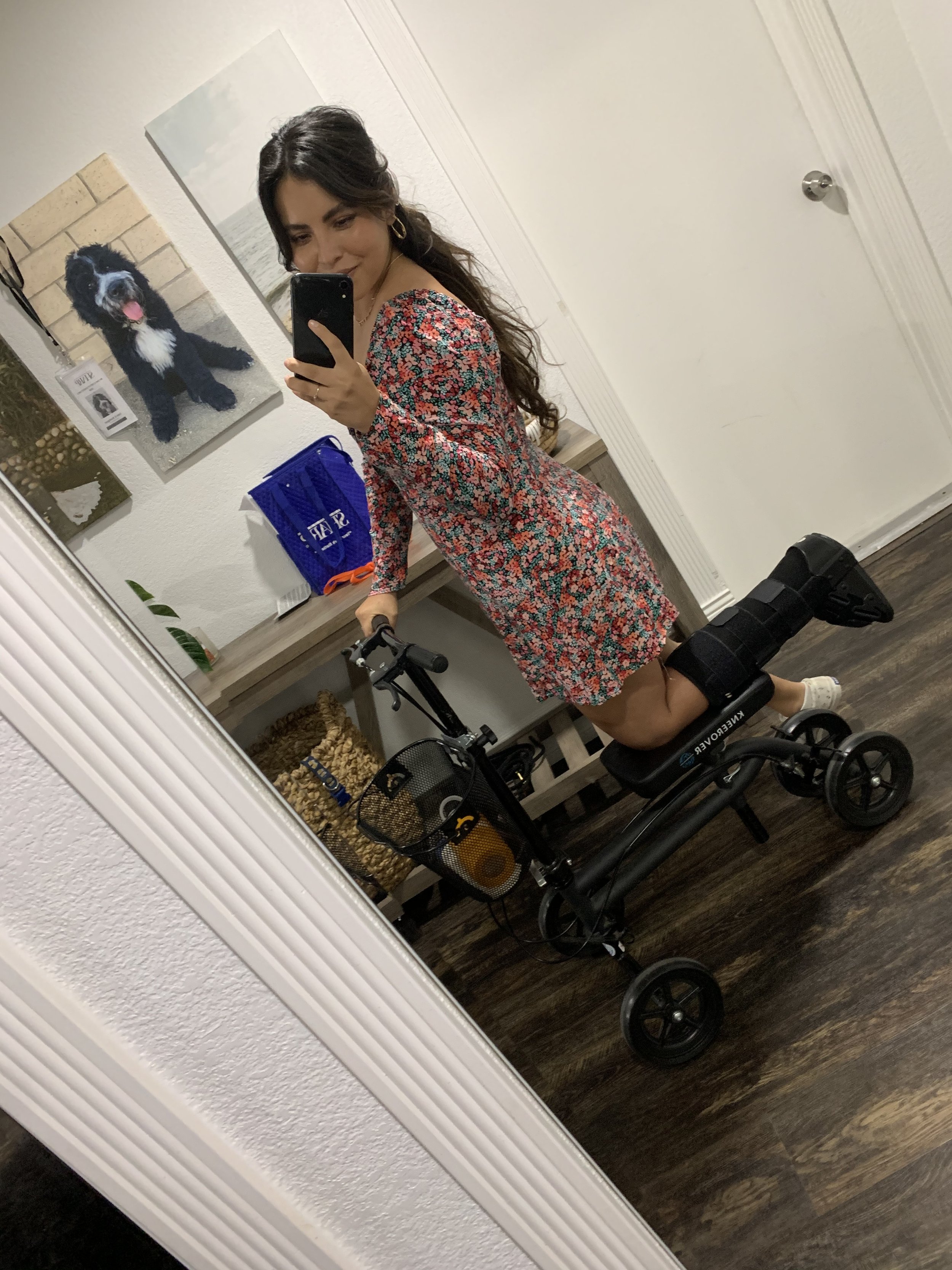 A woman taking a mirror selfie with a smartphone, in a room with wall art, a blue shopping bag, and a mobility scooter talking about how and why she started her head spa.