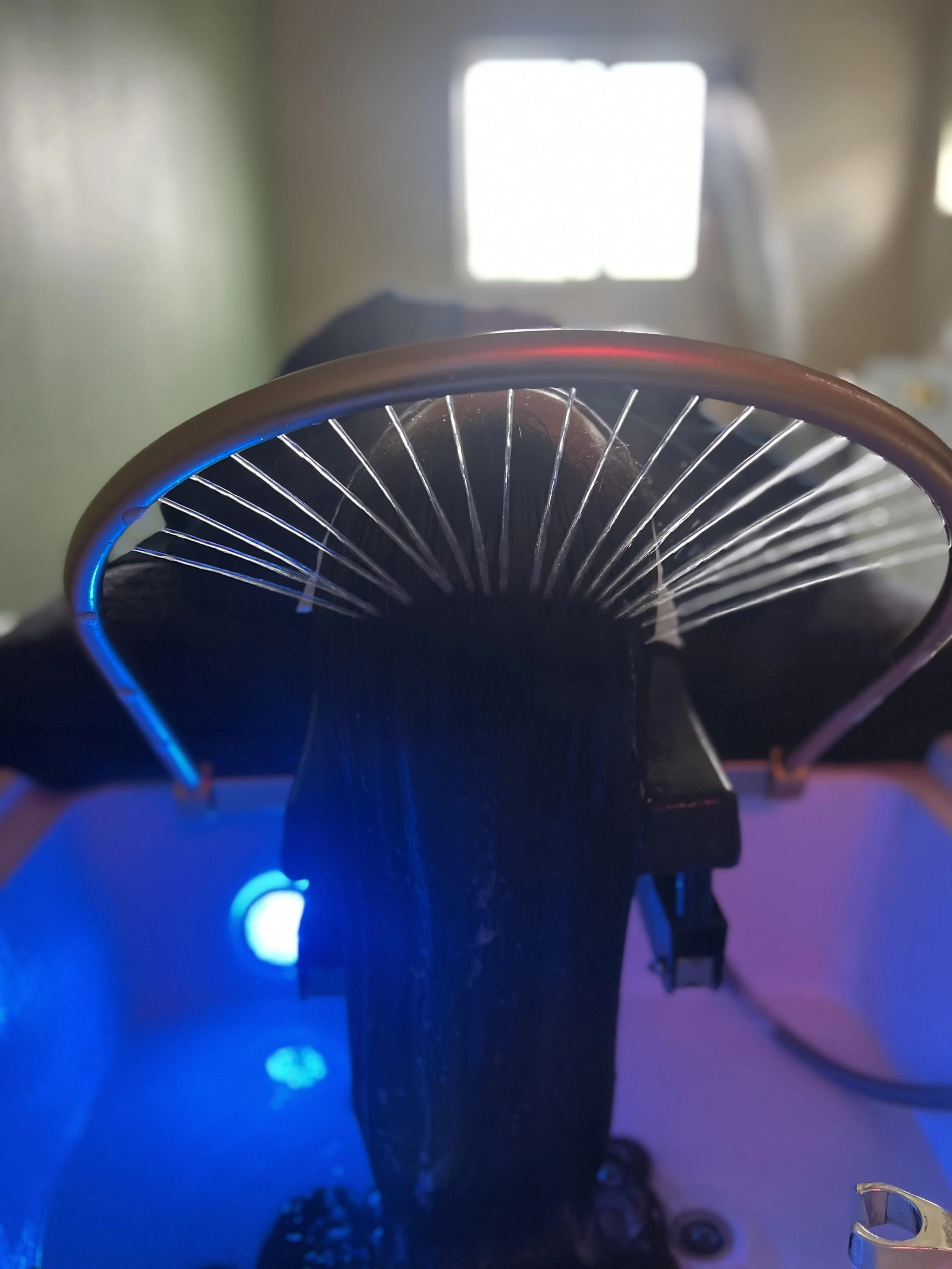 Close-up view of a water circulation with illuminated spokes, with a chair and a window in the background, in a head spa room with colored lighting.
