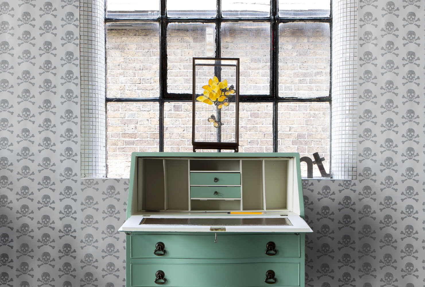 silver glitter skulls wallpaper hand printed and surrounding green vintage writing desk scene in London industrial loft apartment