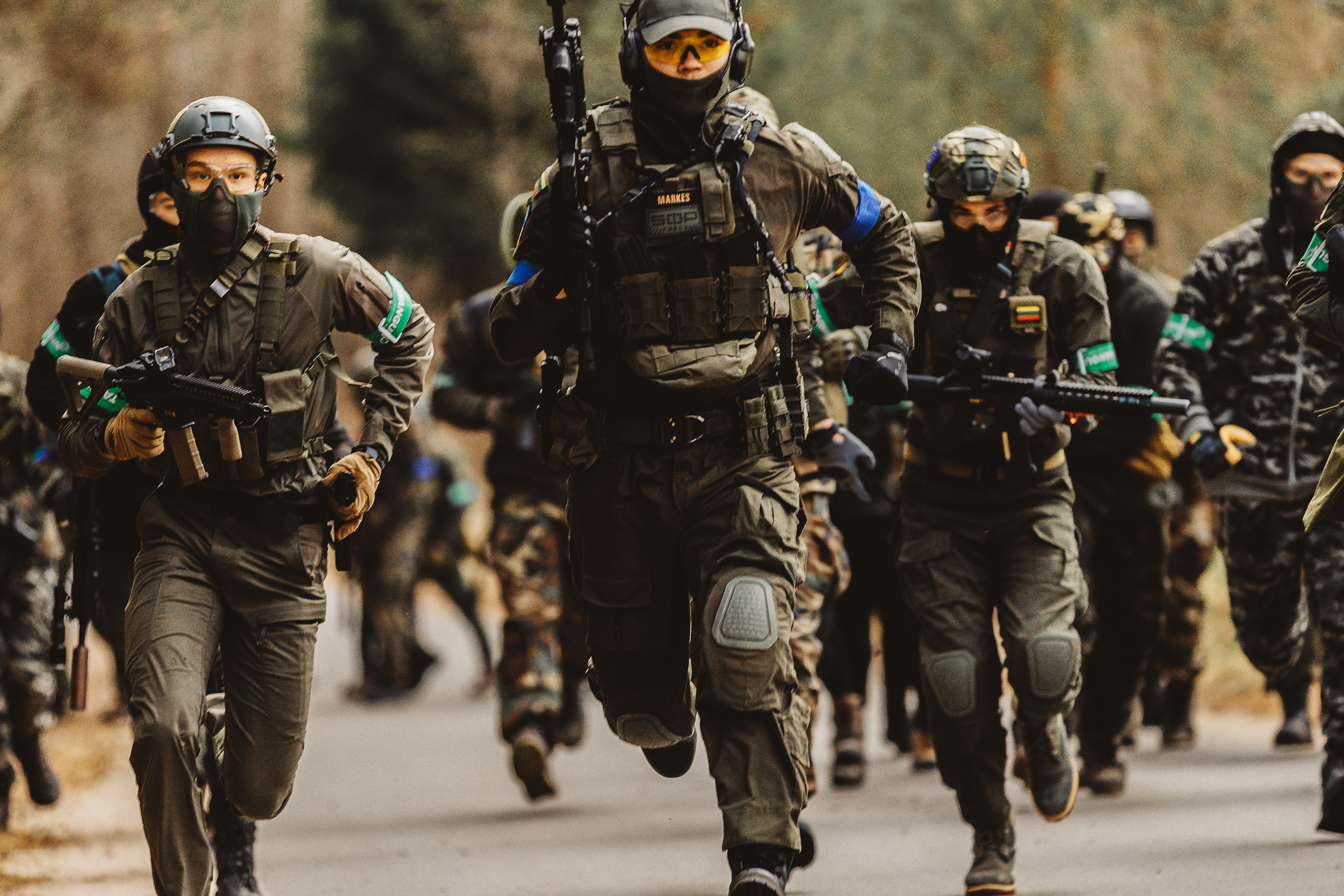 A group of soldiers in combat gear running outdoors on a paved path surrounded by trees.