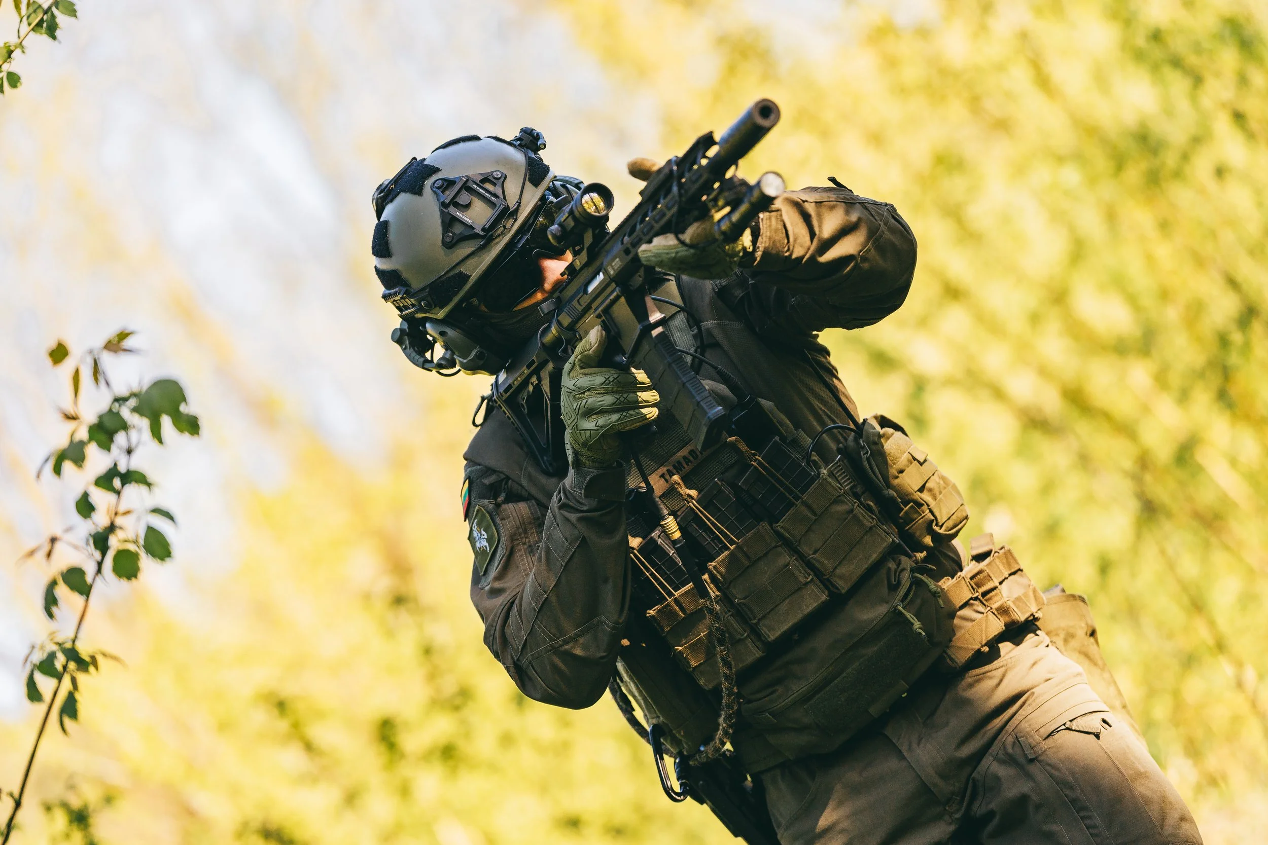 Soldier in tactical gear aiming rifle in forest setting.
