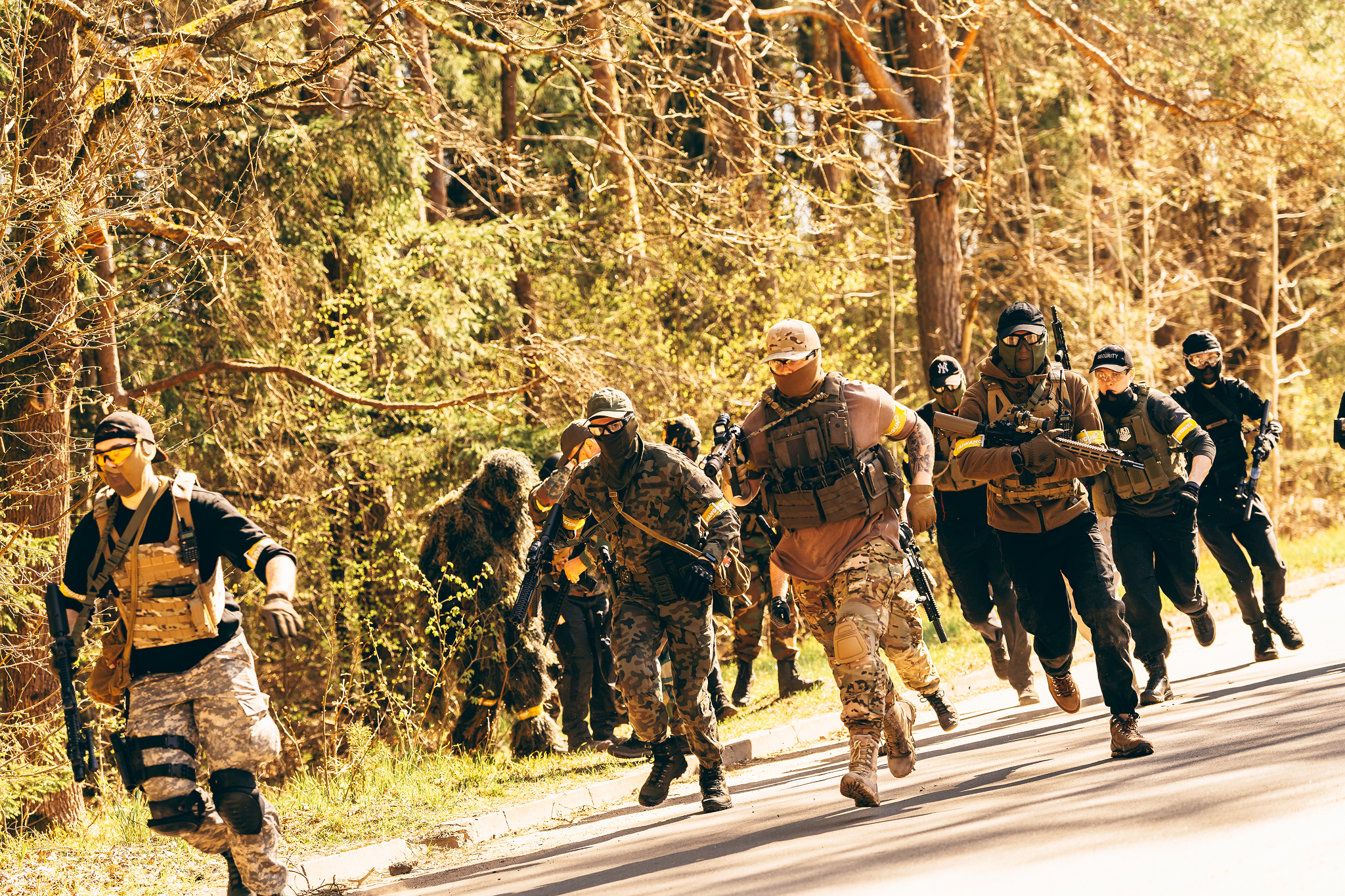 Group of soldiers in tactical gear running on a road through a wooded area during daytime.