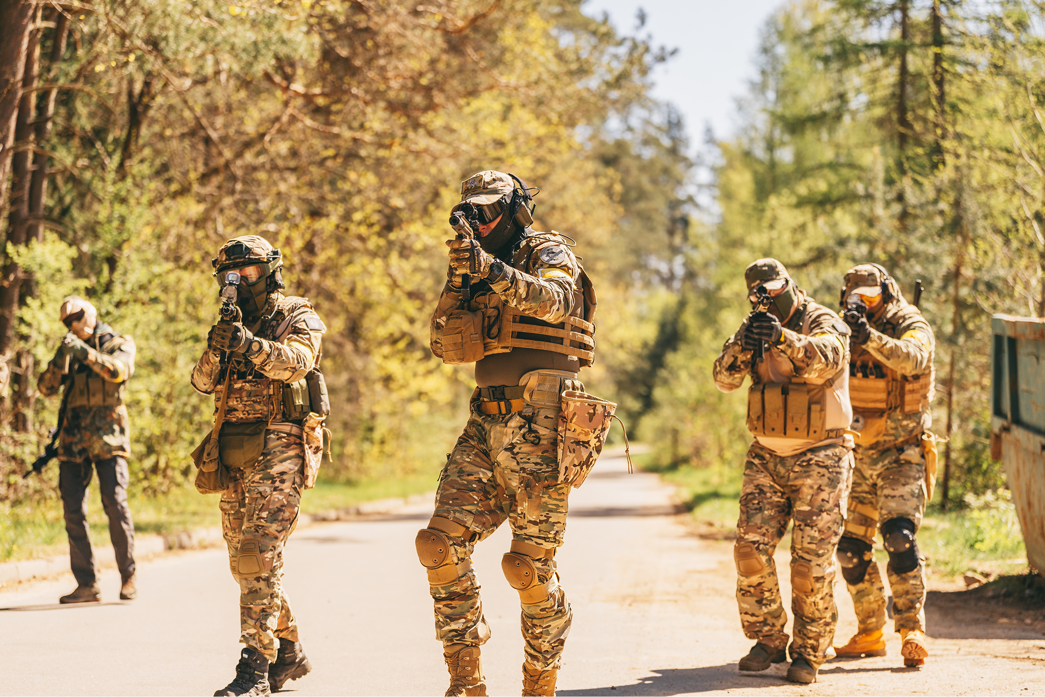 Military soldiers in camouflage uniform with tactical gear and weapons patrolling on a wooded trail.