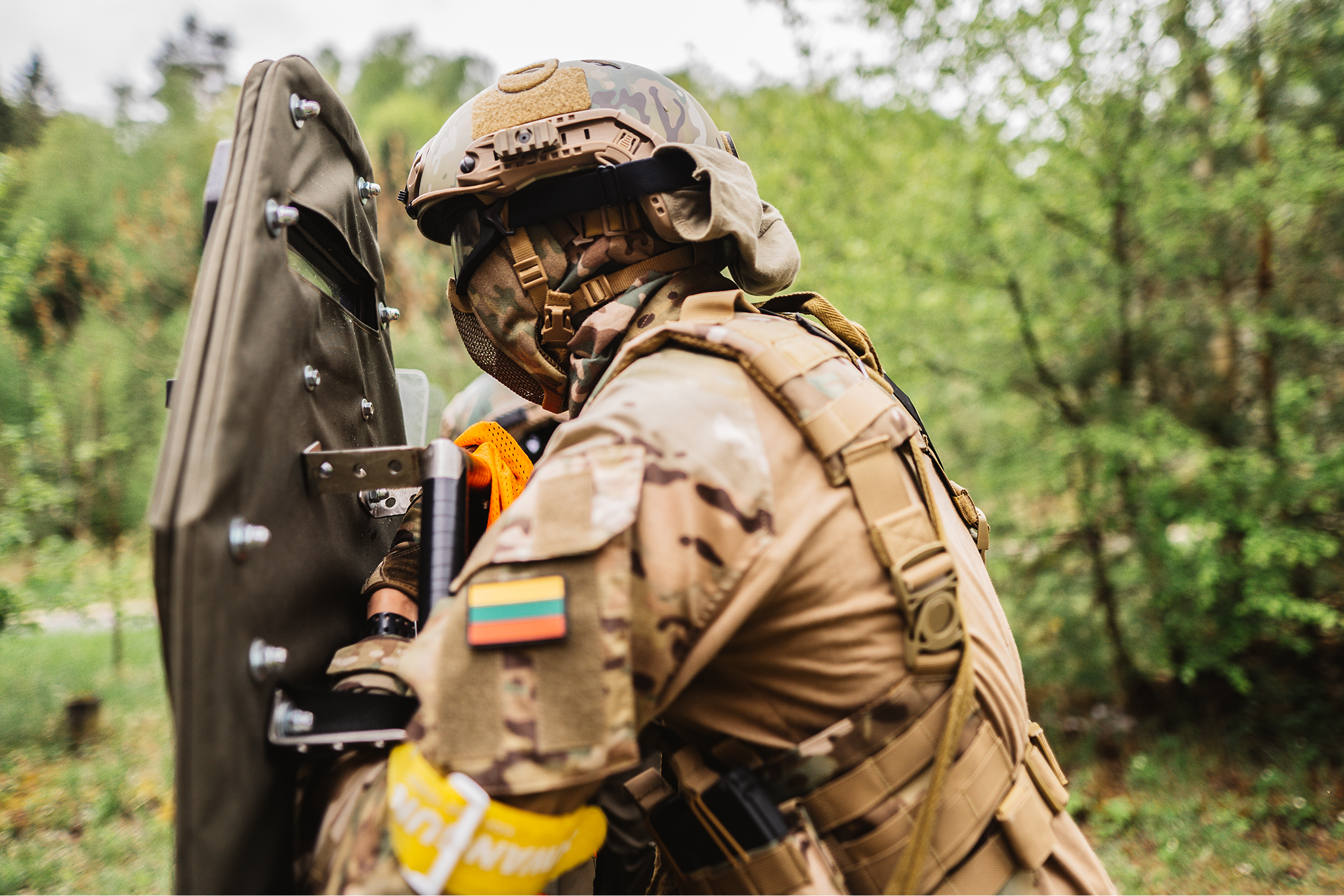 A soldier in camouflage military gear operating a shield during a training exercise outdoors.