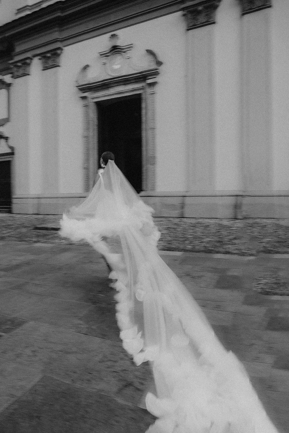 Bride in long veil style and holding the veil in a romantic church front