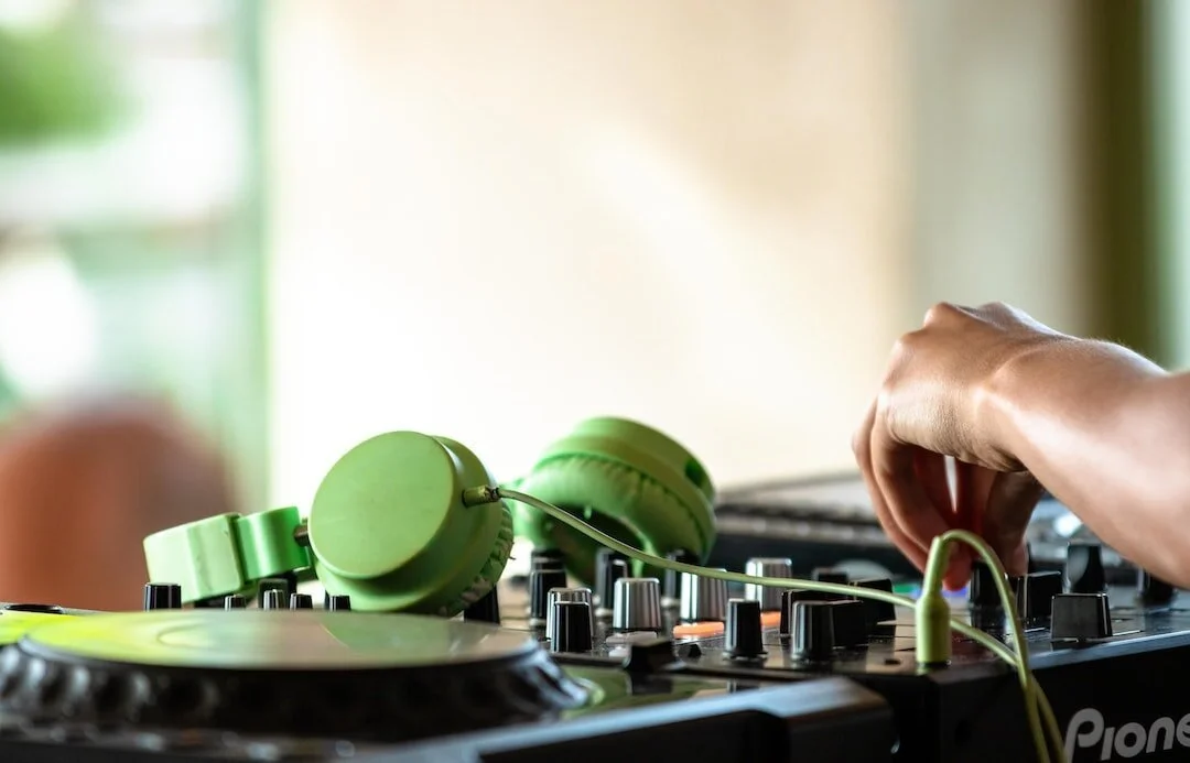 Green headphones on a DJ mixer with a hand reaching to adjust controls.