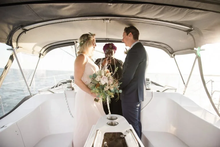 Bride and groom exchanging vows on a boat with an officiant taking photos.