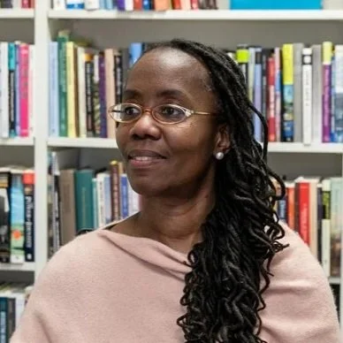 A woman with glasses and long, curly hair standing in front of a bookshelf filled with books.