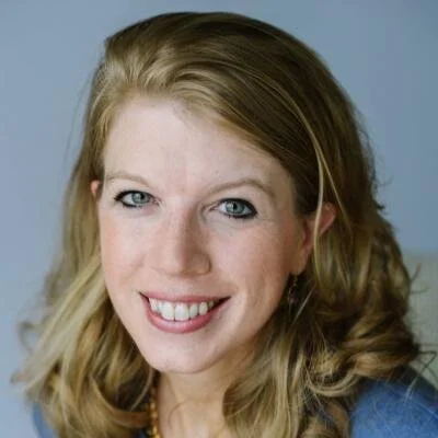 Close-up portrait of a smiling woman with wavy blonde hair and blue eyes.