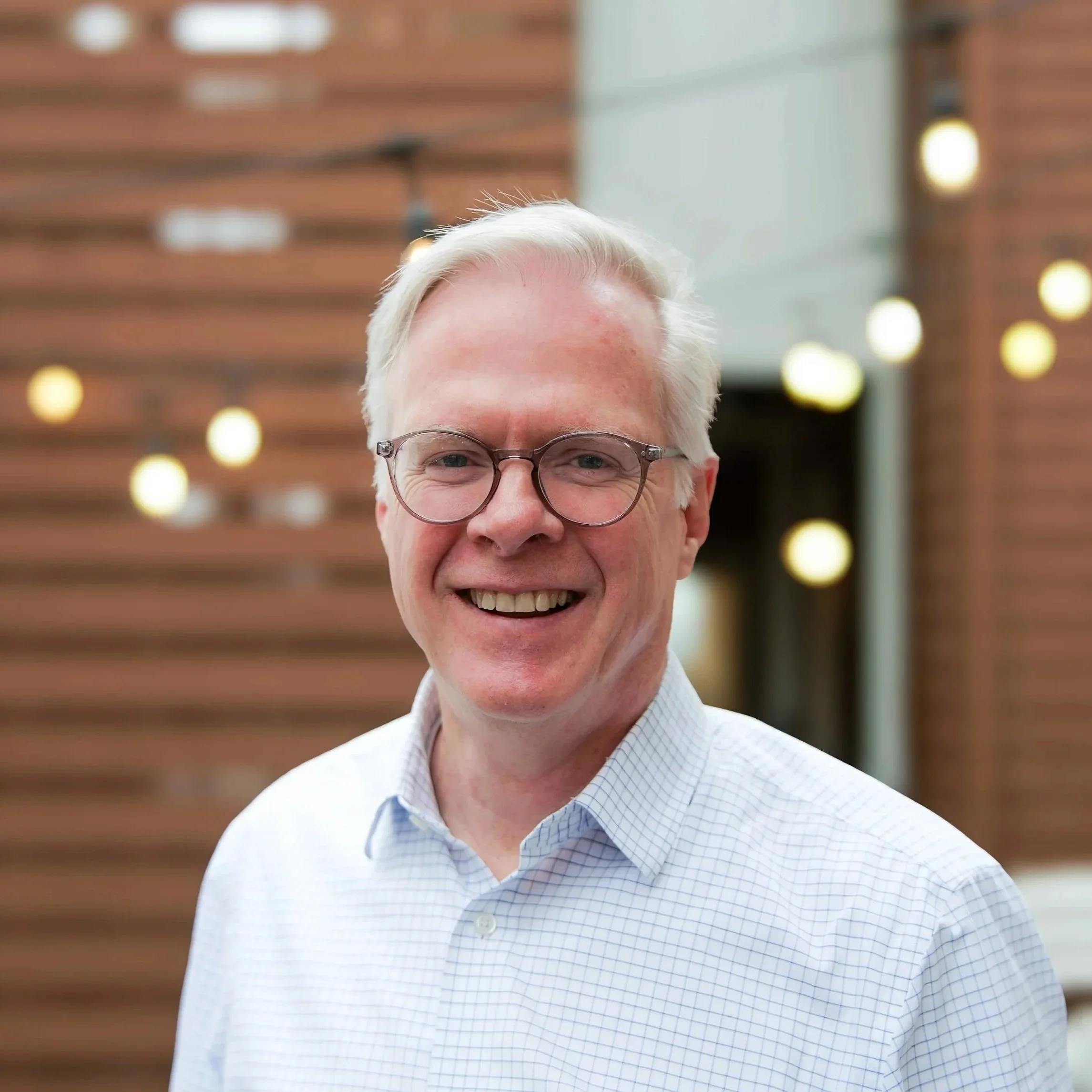 Smiling man with glasses in outdoor setting.