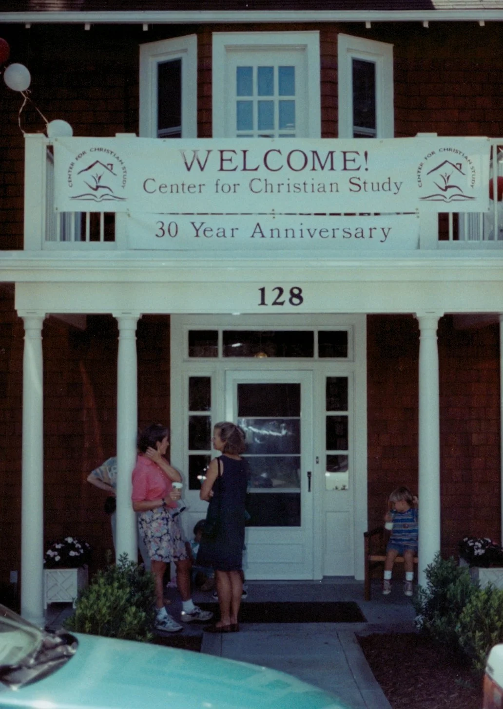 A building with a sign celebrating the 30th anniversary of the Center for Christian Study, with people standing and sitting in front.