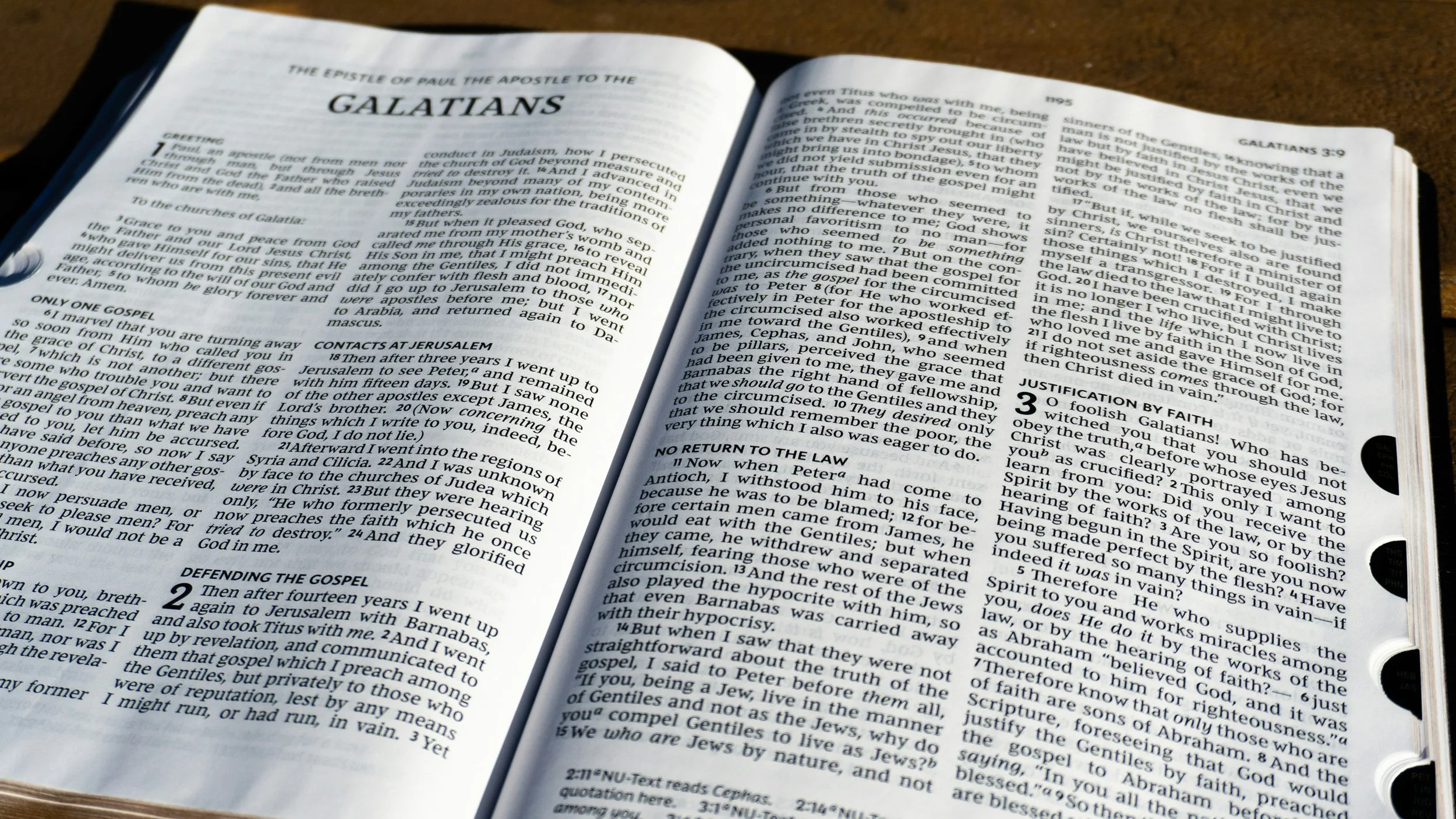 Open Bible to Galatians chapter 3 and 4, with pages spread open on a wooden table.