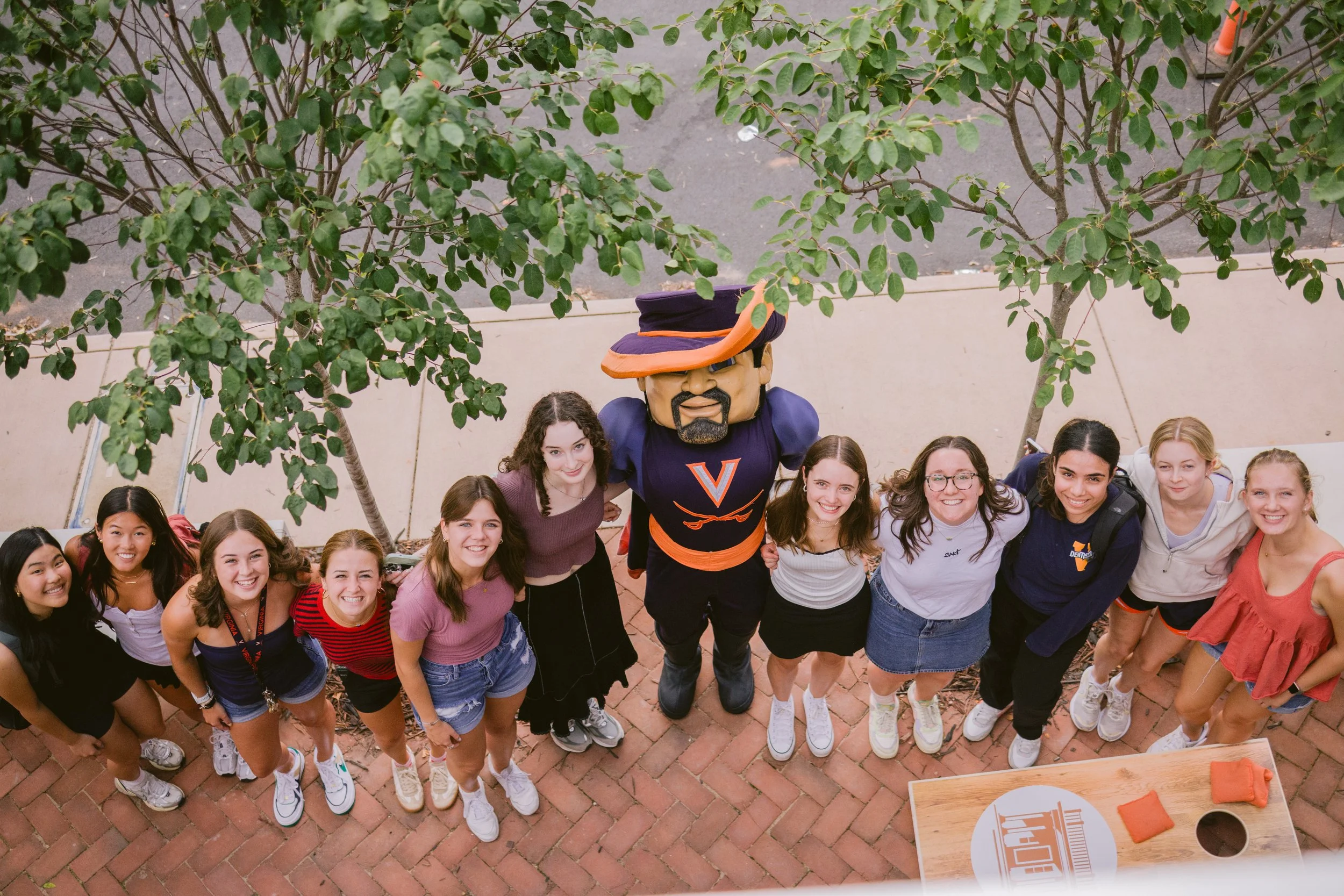 Group of young women and a mascot in a U-Va. shirt posing for a photo outdoors under trees