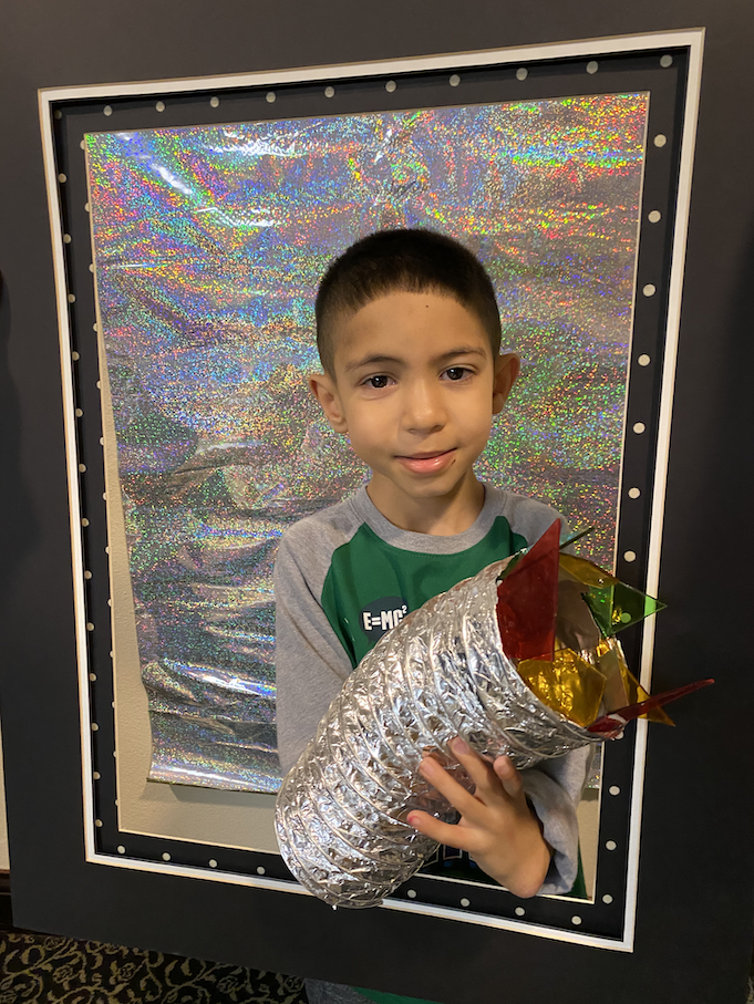 A young boy holds up a silver tube with chunks of different color chunks of plastic..png
