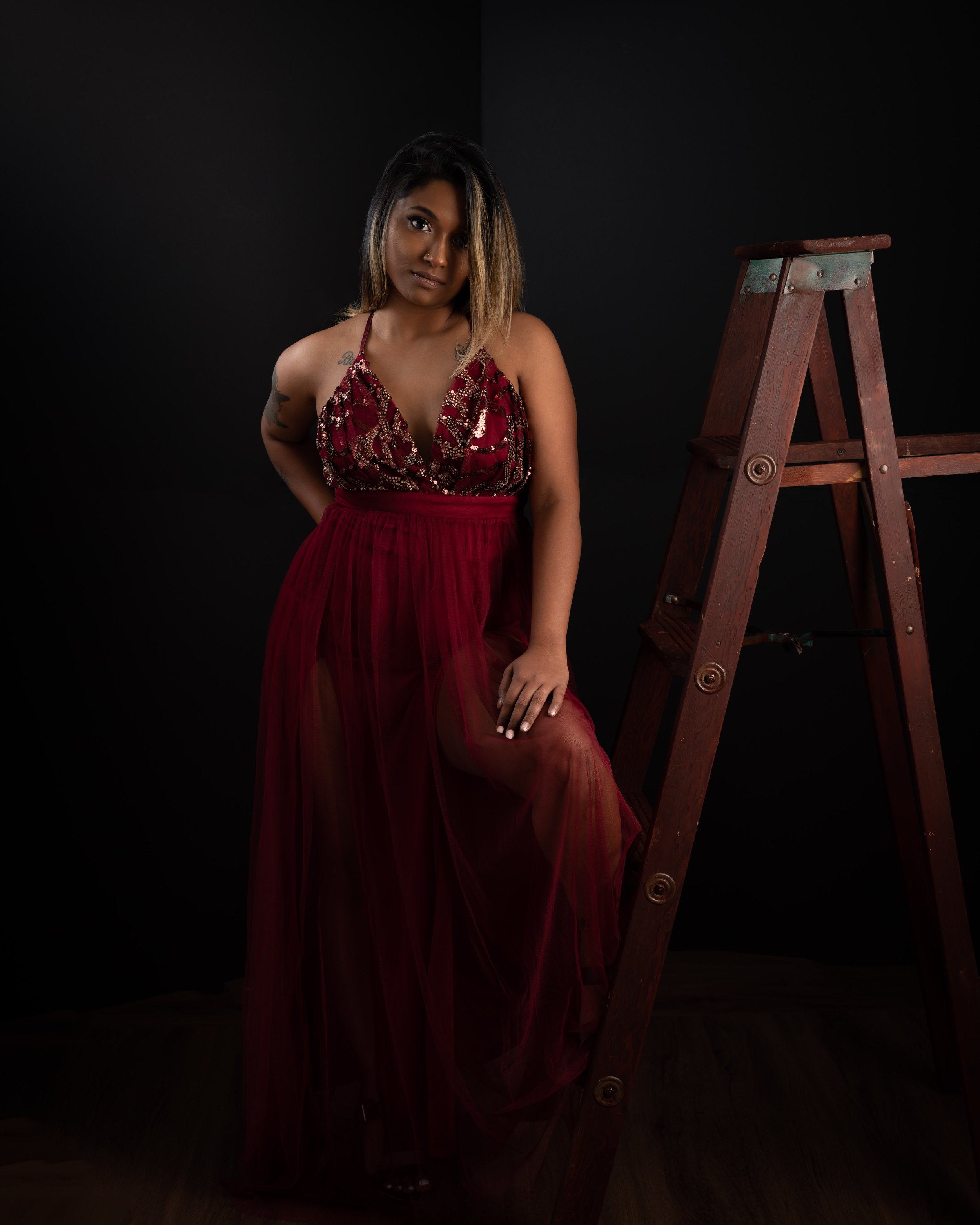 Beautiful Glamour Portrait of a Indian woman in a burgundy dress with one leg on a ladder while she strike a pose