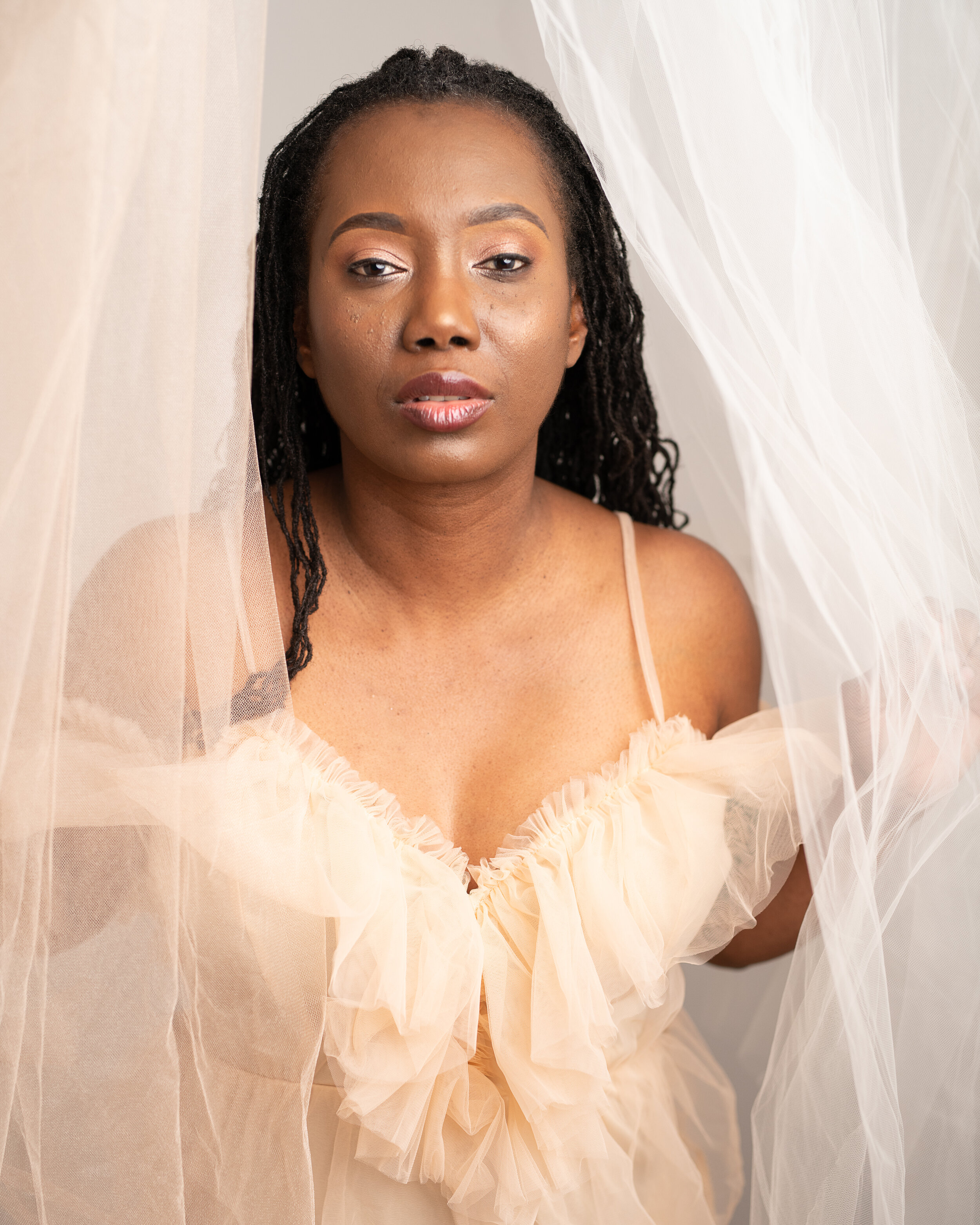A sensual glamour portrait of a woman with a beige short dress with beige and white tulle draped around her
