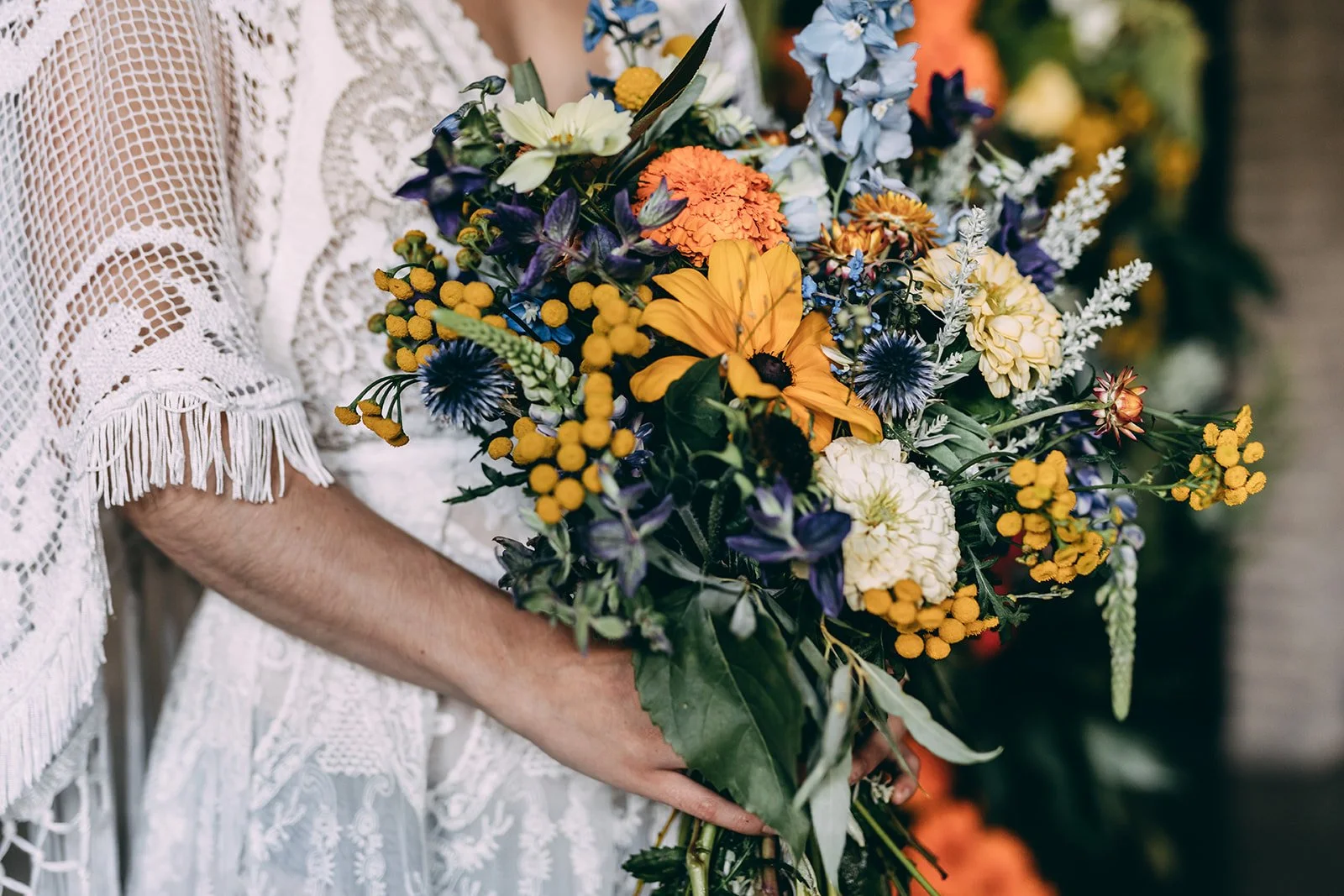 Person dressed in white lace holding a colorful bouquet of flowers