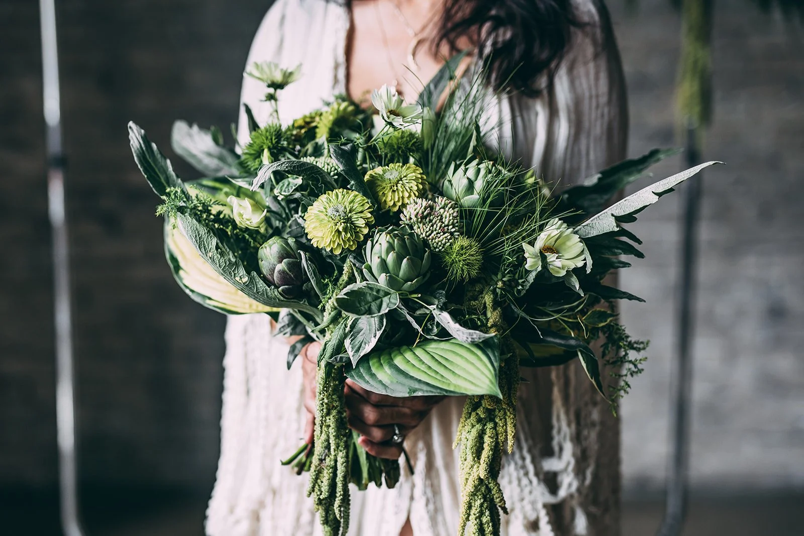 A woman holding a large bouquet of green and white flowers with dark leaves.