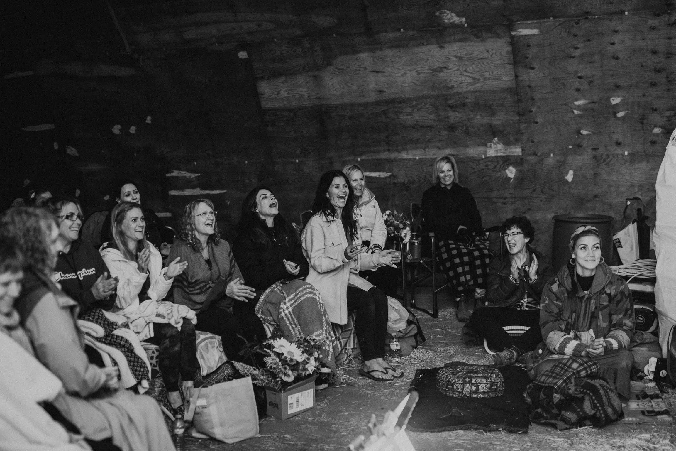 A group of women sitting and standing in a rustic wooden room, laughing and enjoying each other's company.