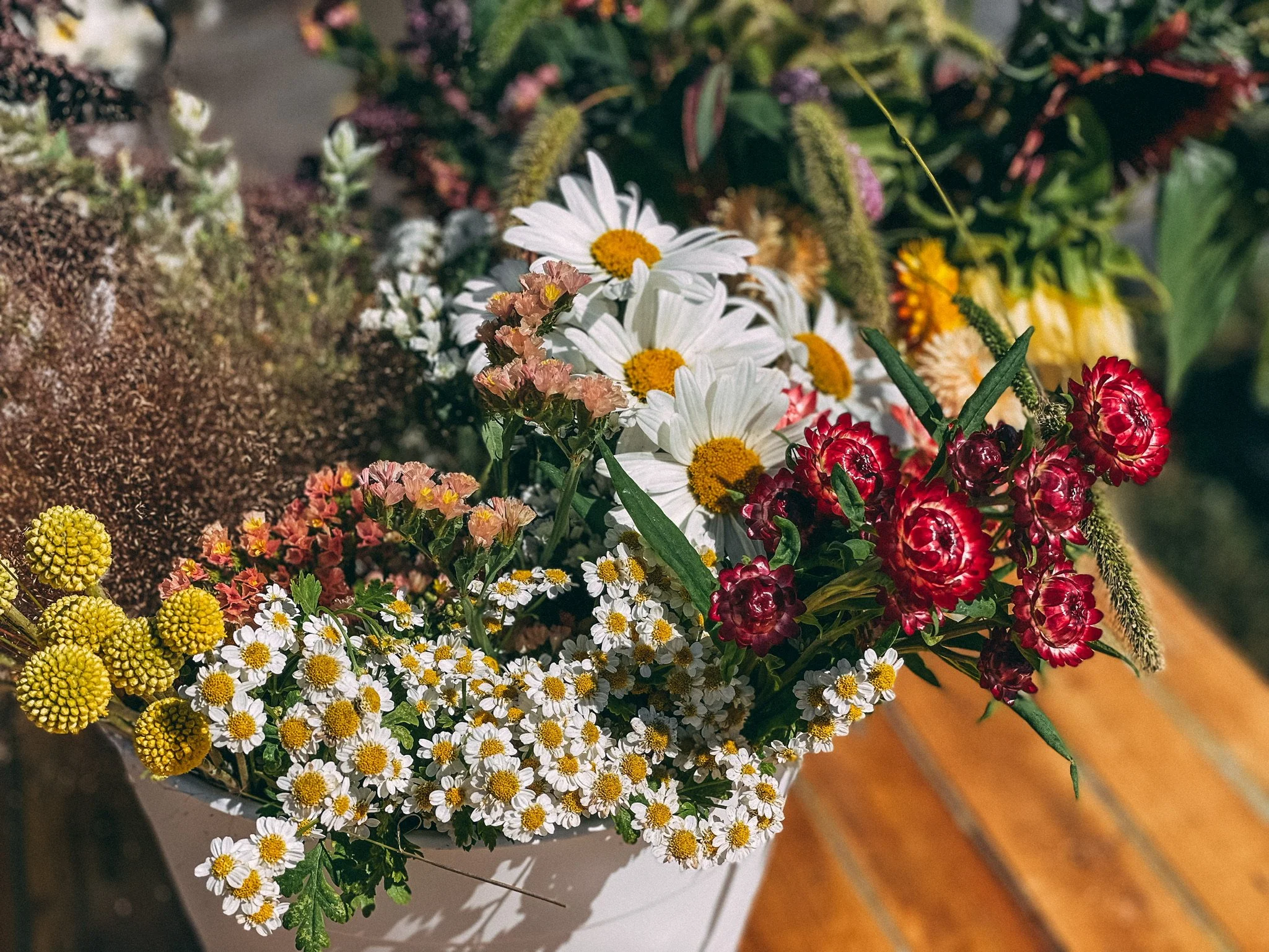 Assorted fresh flowers, including daisies, small yellow cluster flowers, pink, red and purple blooms, arranged in a bouquet.