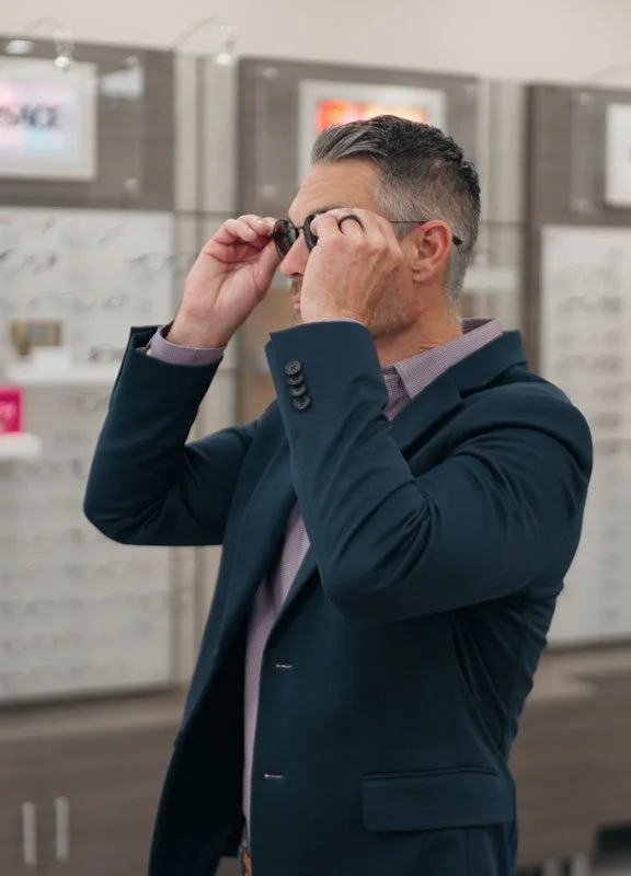 A man in a dark suit trying on glasses in an eyewear store in Redding, CA at Blink Optometry.