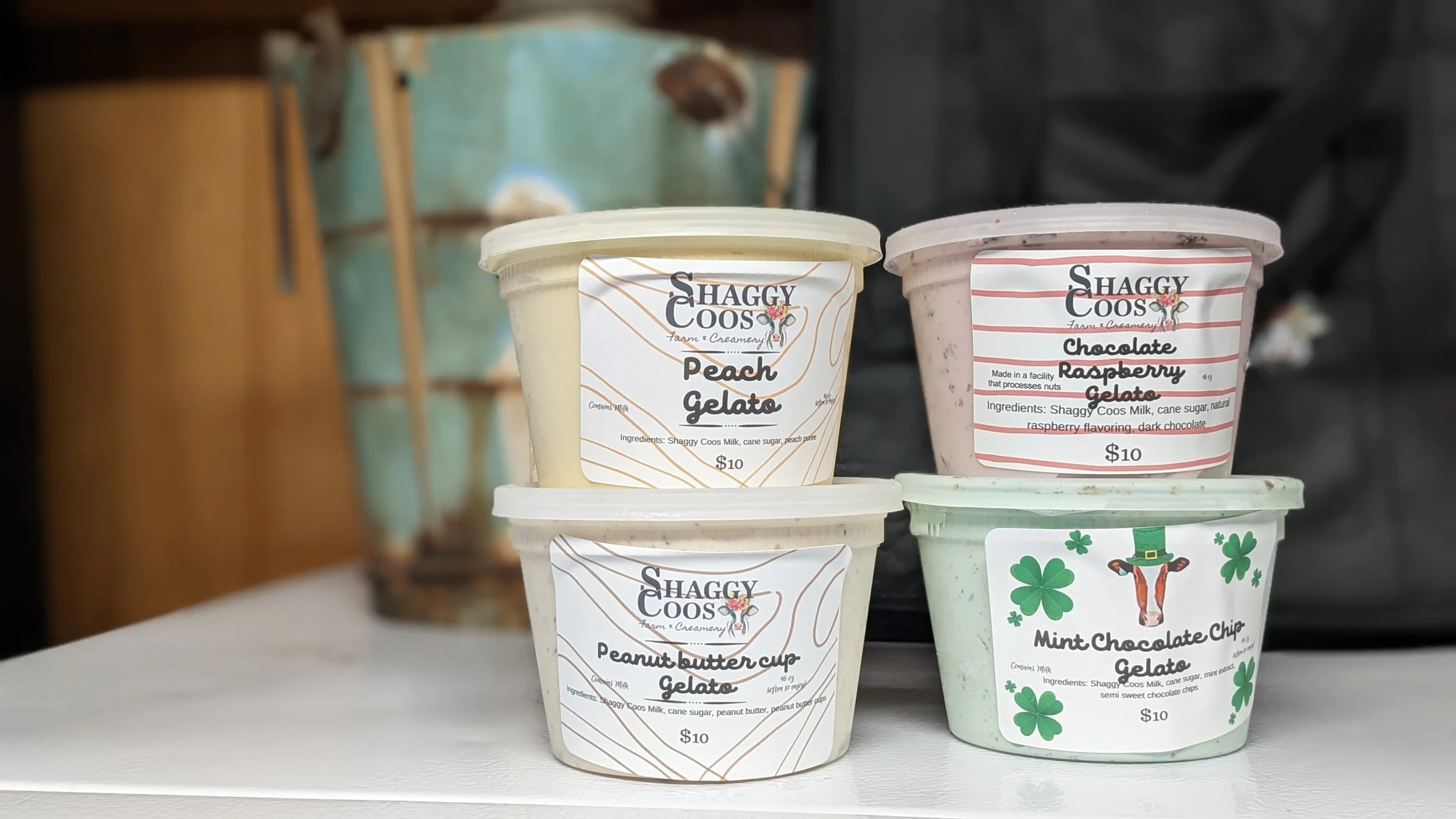 Four containers of gelato with different flavors and labeled with brand and ingredients, including peach gelato, chocolate raspberry gelato, peanut butter cup gelato, and mint chocolate chip gelato.