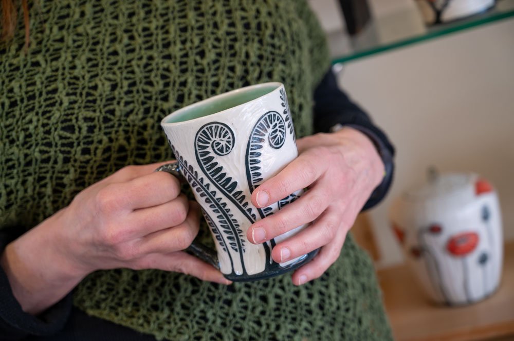 Molly holding one of her mugs featuring a fern design
