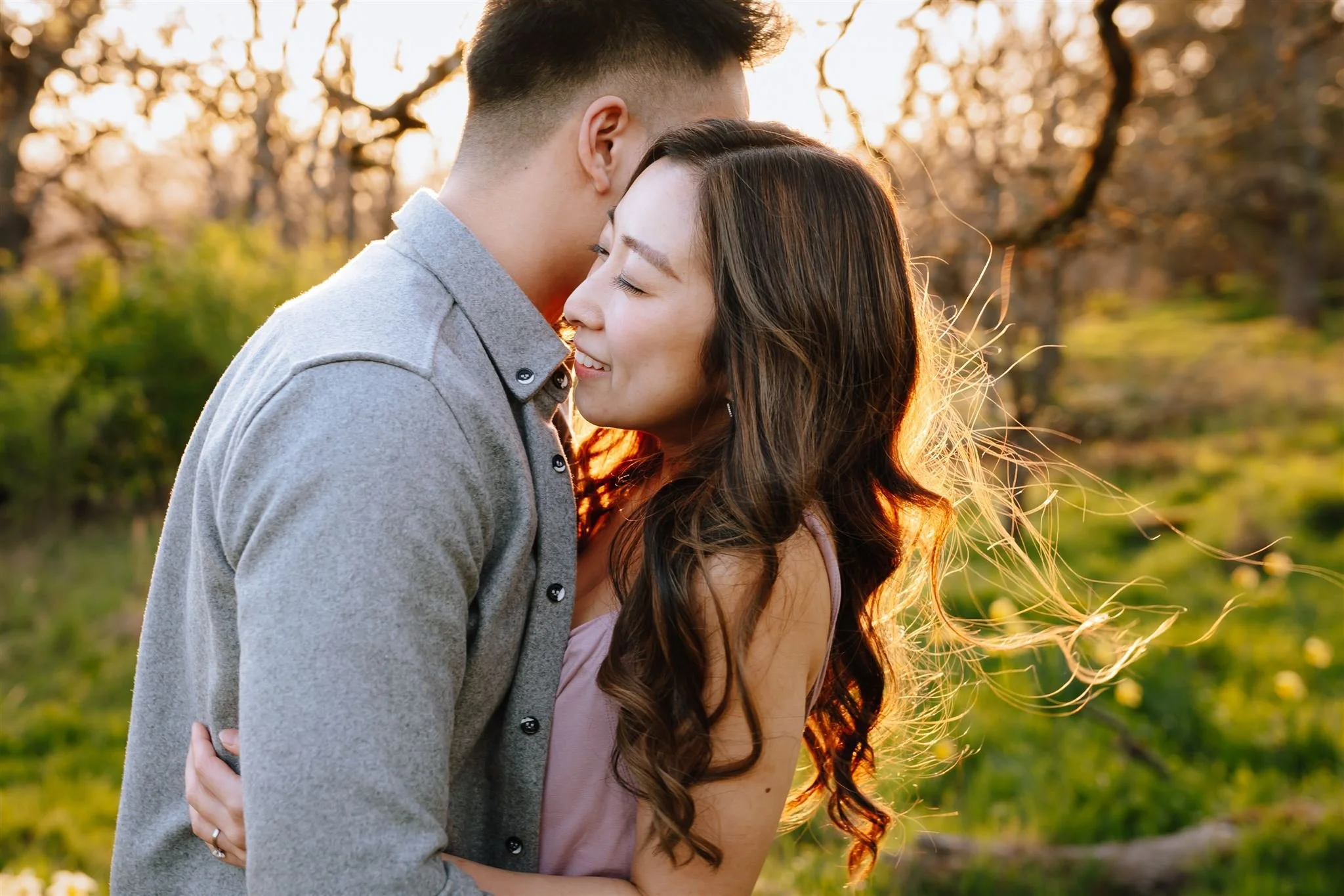 A couple hugging outdoors during sunset with trees in the background.