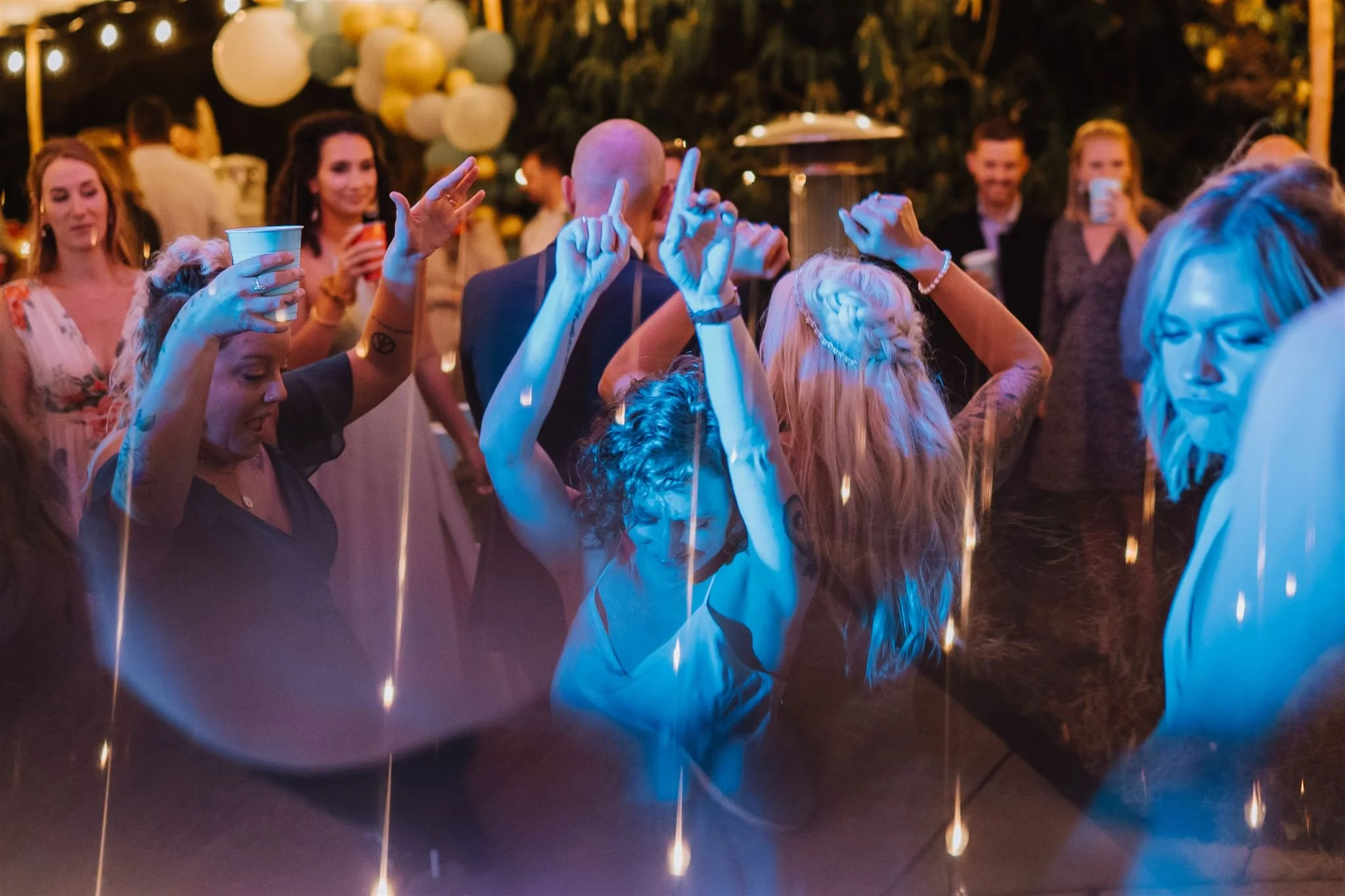People dancing at a nighttime outdoor party with string lights and balloons, enjoying the music and celebration.