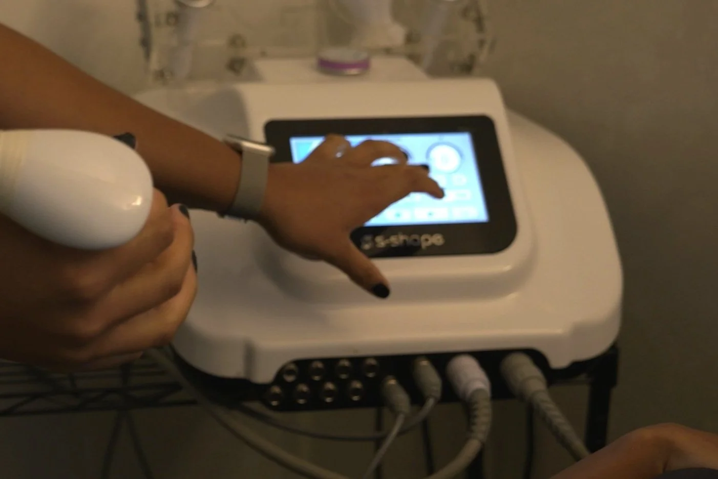 A person using a medical ultrasound machine with a handheld probe, touching the screen of the device.