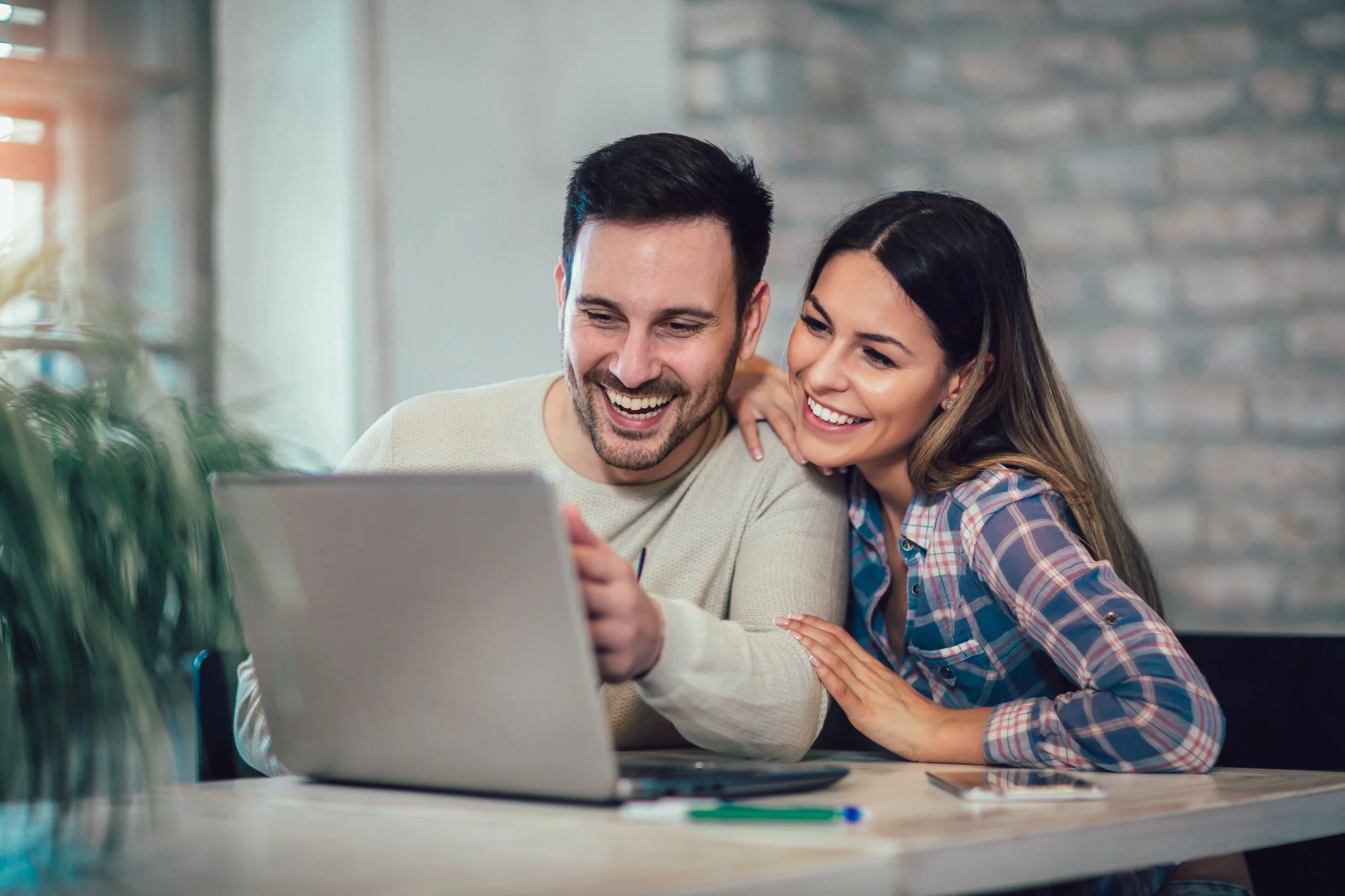 A young man and woman sitting at a table, looking at a laptop and smiling together.