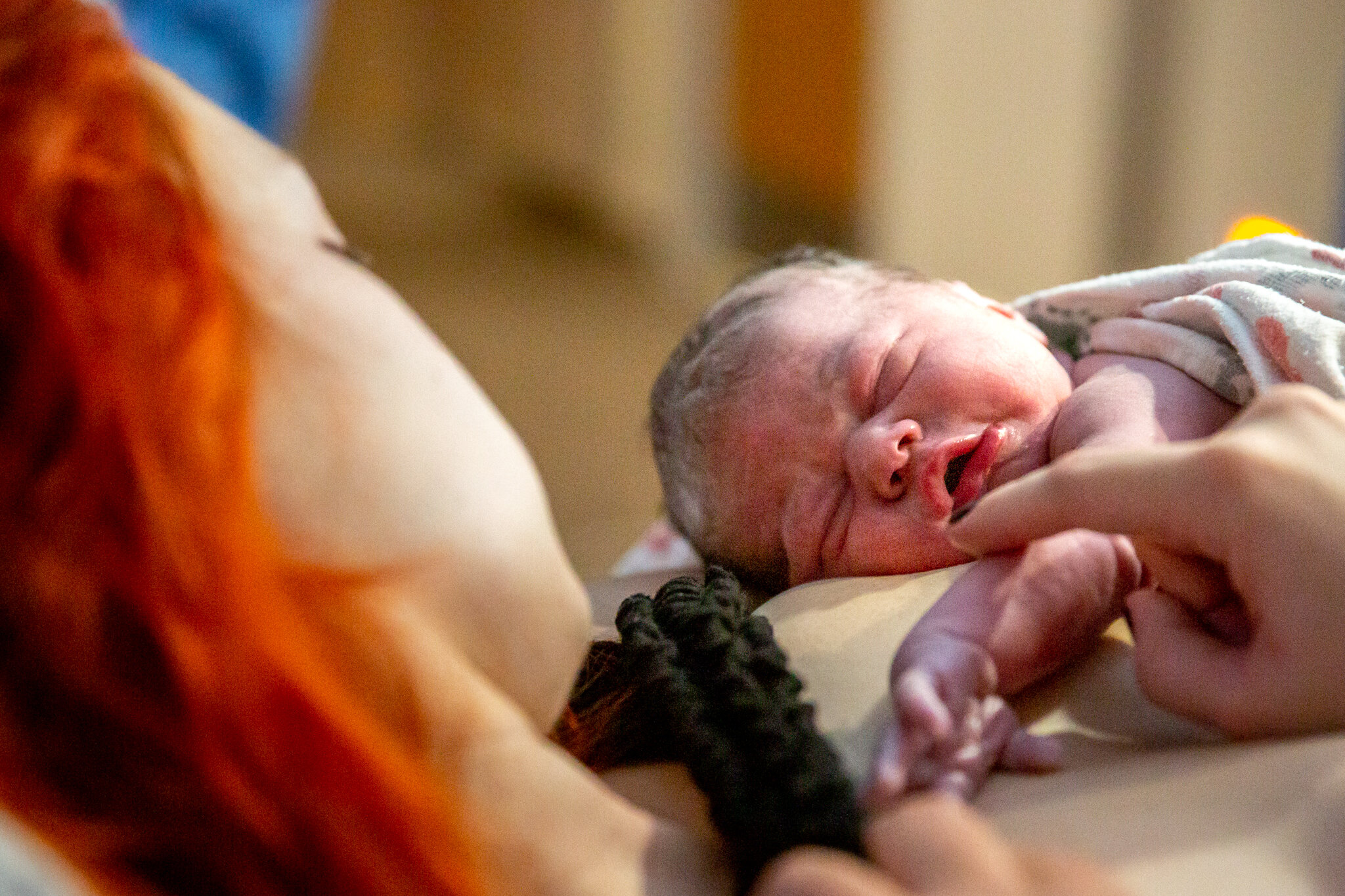 Woman stroking newborn baby's arm as she sleeps on her chest