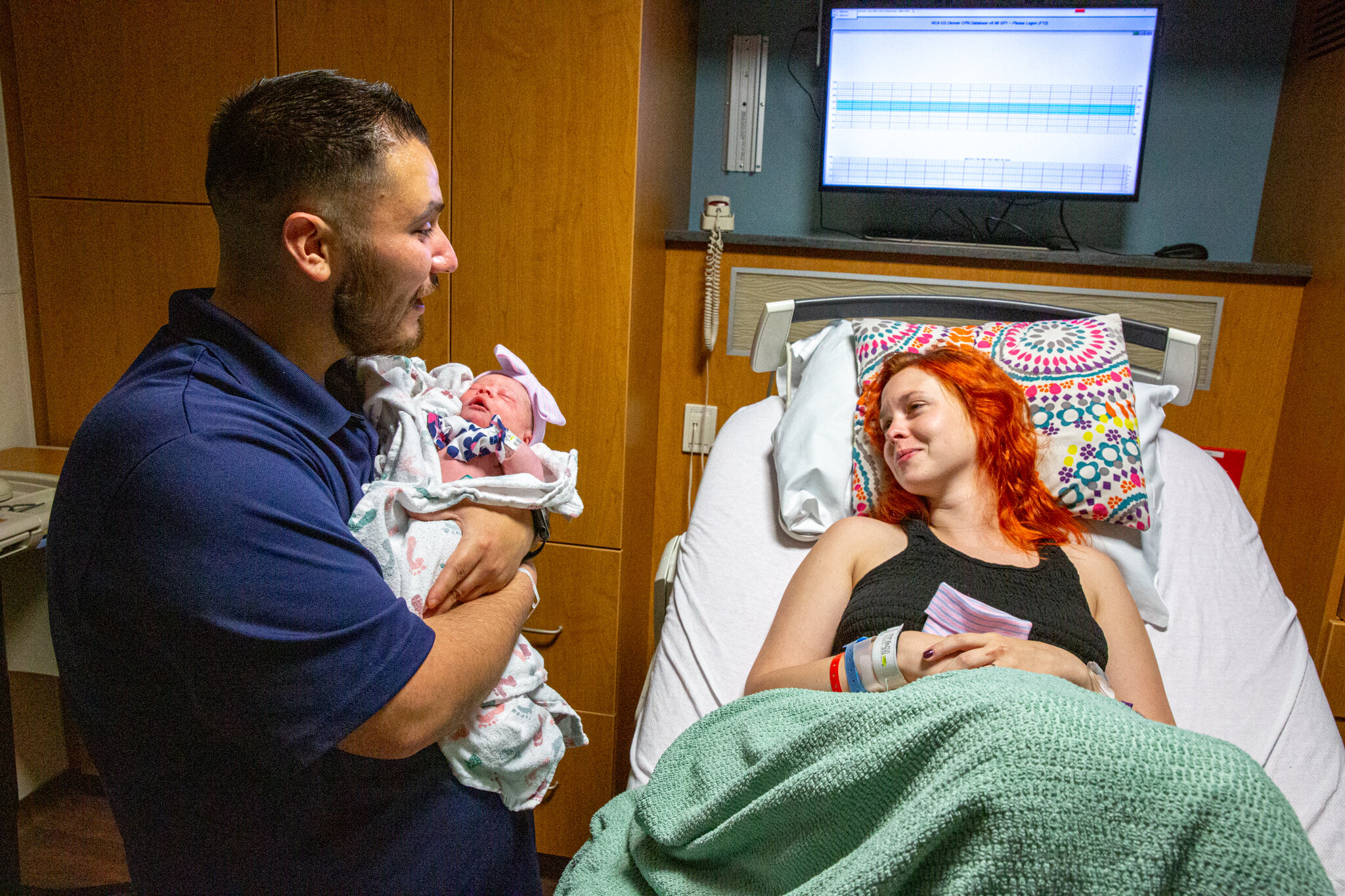 Dad holding baby and mom is hospital bed laughing