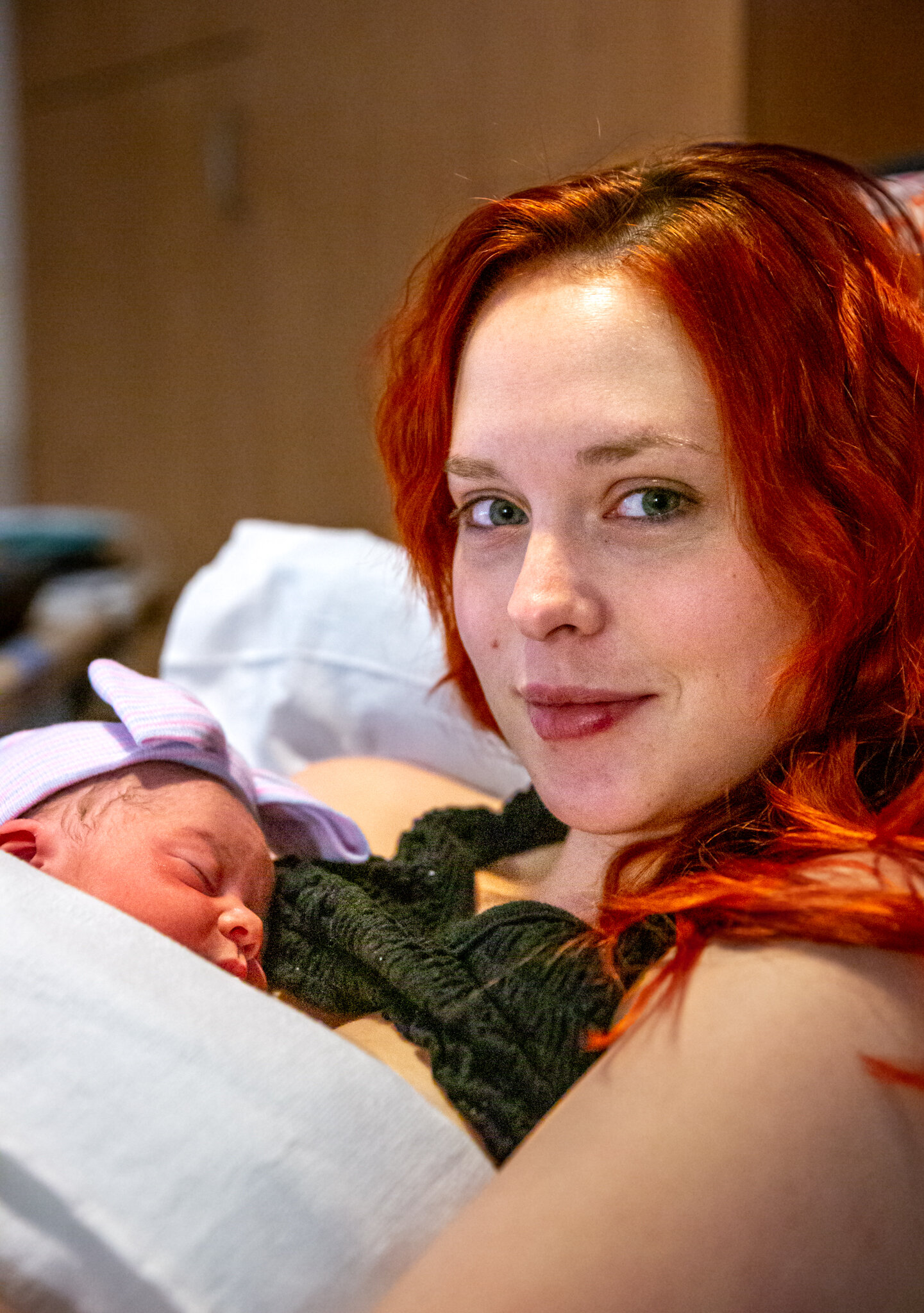 Woman smiling at camera, baby asleep on chest