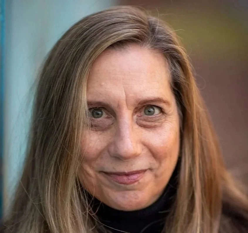 Marsha, with blonde-brown hair, staring right at the camera with a blue and faded orange background.