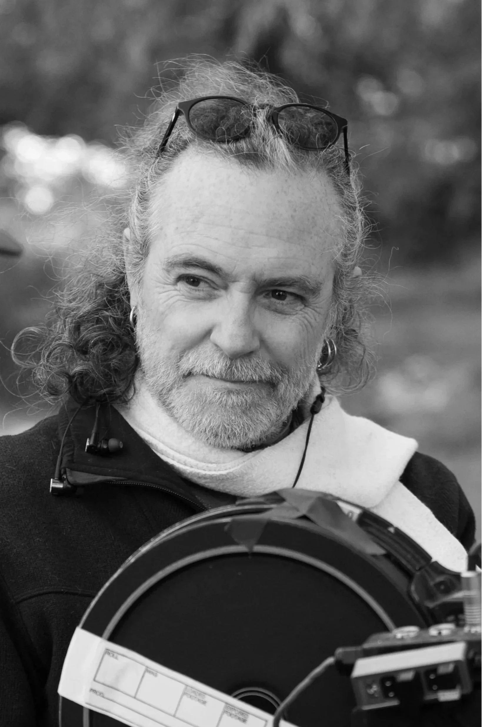 Black and white photo of David wearing sunglasses on his head, a white scarf, and holding a film canister.