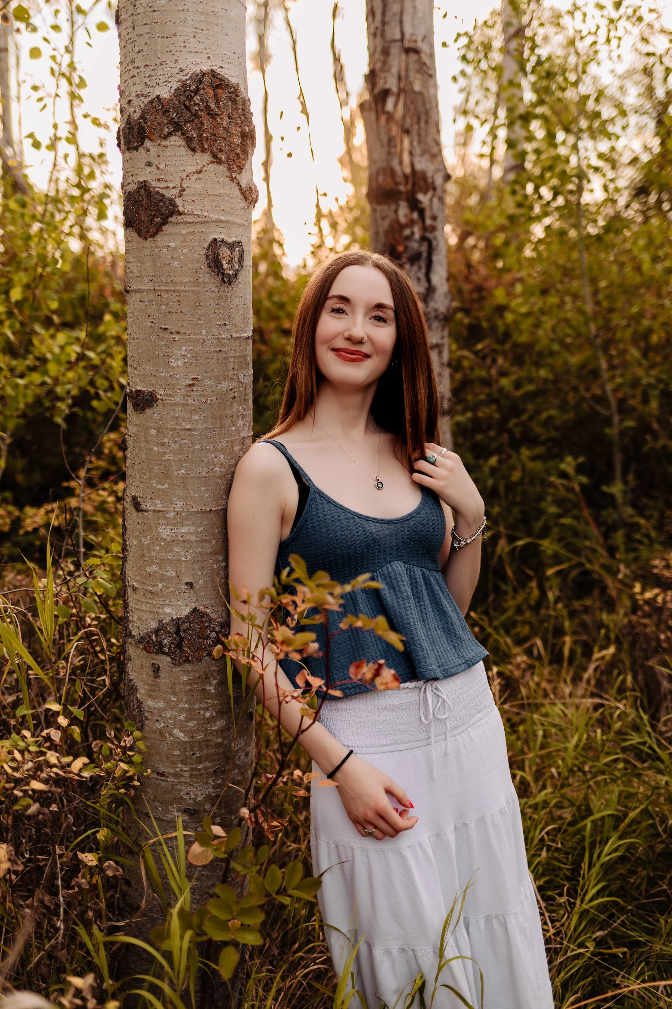 A family of three, a man, a woman, and a young girl, walking hand in hand down a dirt trail in a rural setting during sunset, surrounded by trees and golden grass.