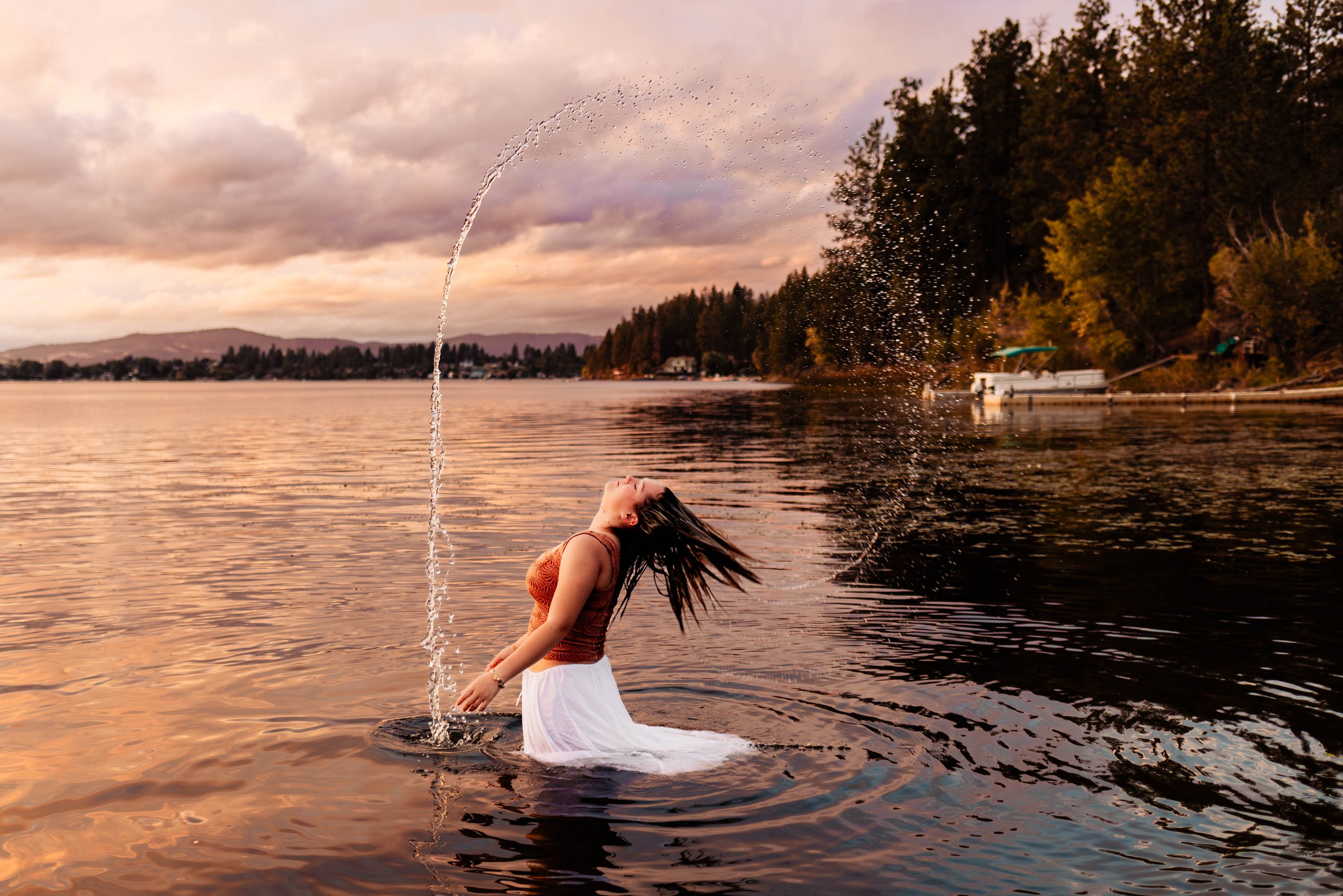 A happy couple embracing by a lakeside during sunset, with mountains and a partly cloudy sky in the background.