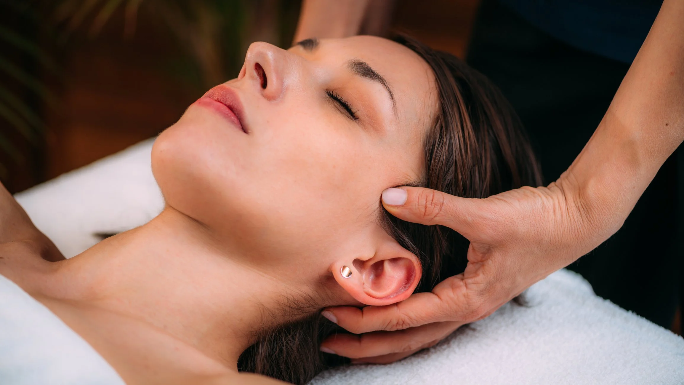 woman's head being cradled by a therapist's hands. woman's eyes are closed as she relaxes