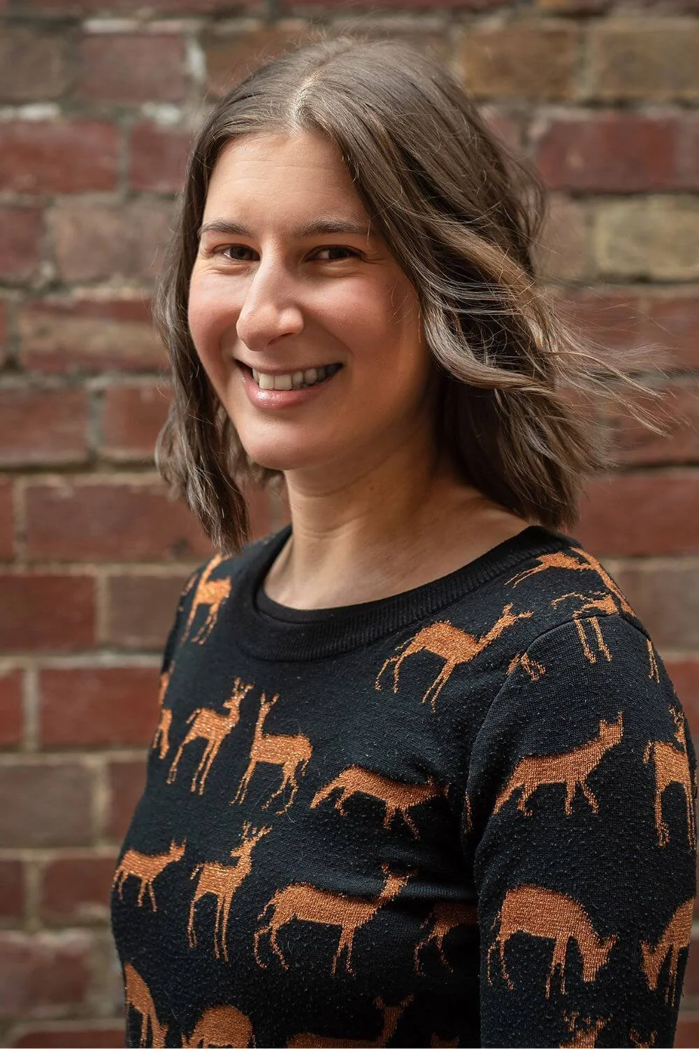 Sarah looking professional smiling at the camera in front of a brick wall