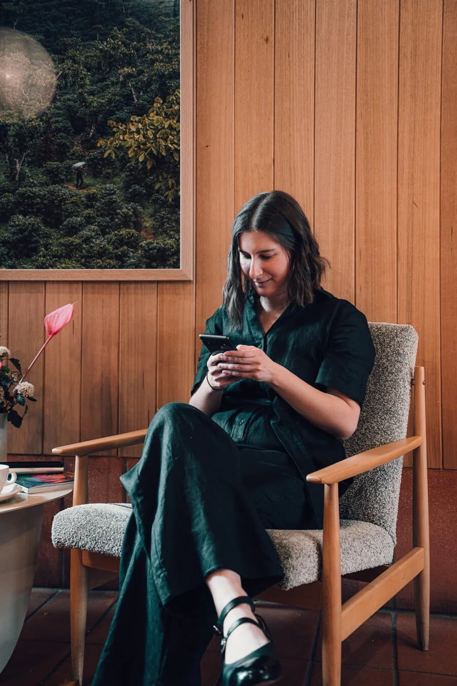 Sarah Marriott providing copywriting services sitting in a warm lit coffee shop on a grey chair looking at her smartphone