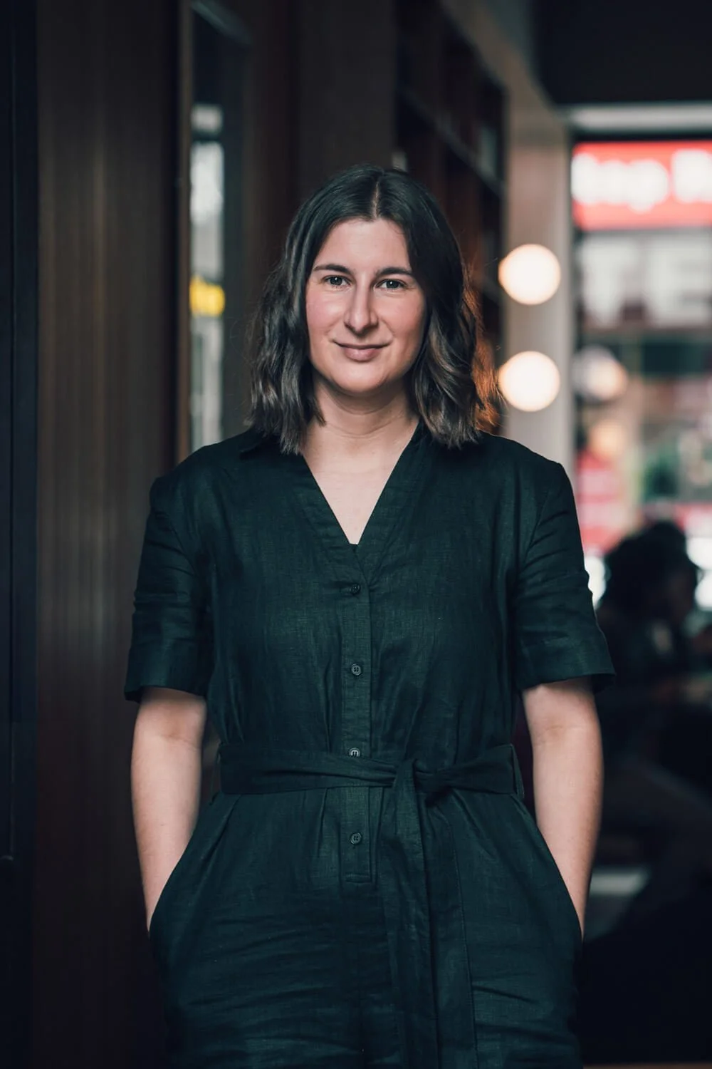 Copywriting services from Sarah Marriott in a warm lit coffee shop, standing up and smiling, wearing black clothes