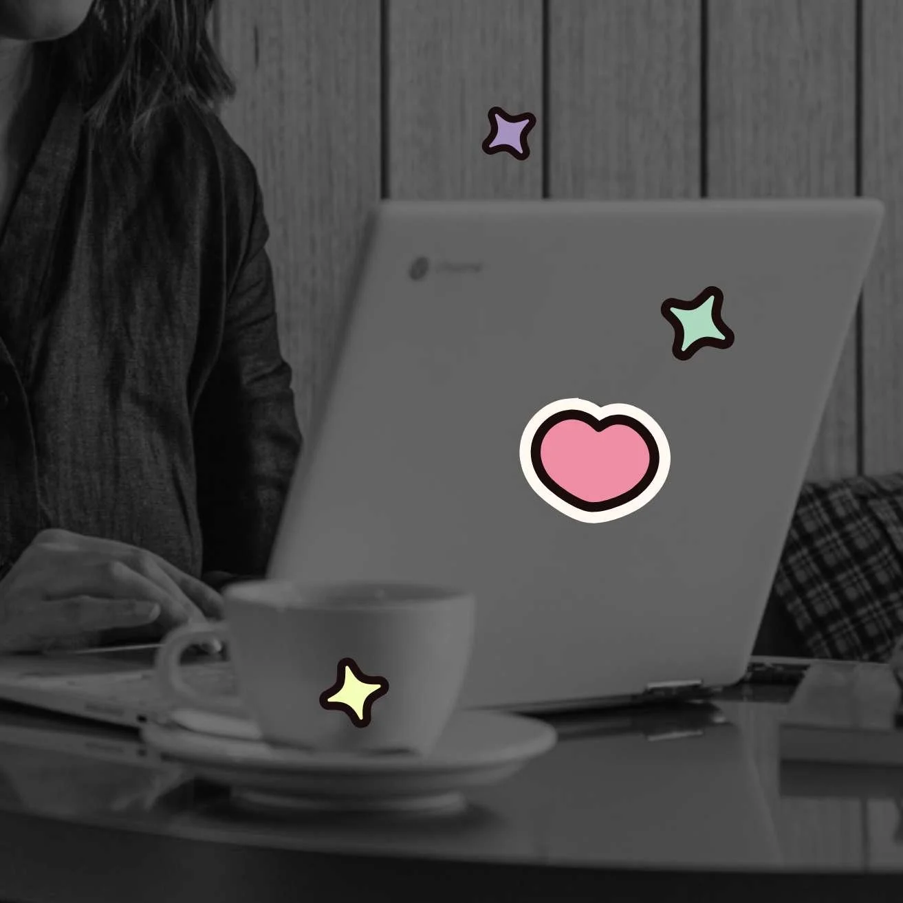 greyscale-style laptop computer and coffee cup with woman sitting at table with colourful heart and star graphics