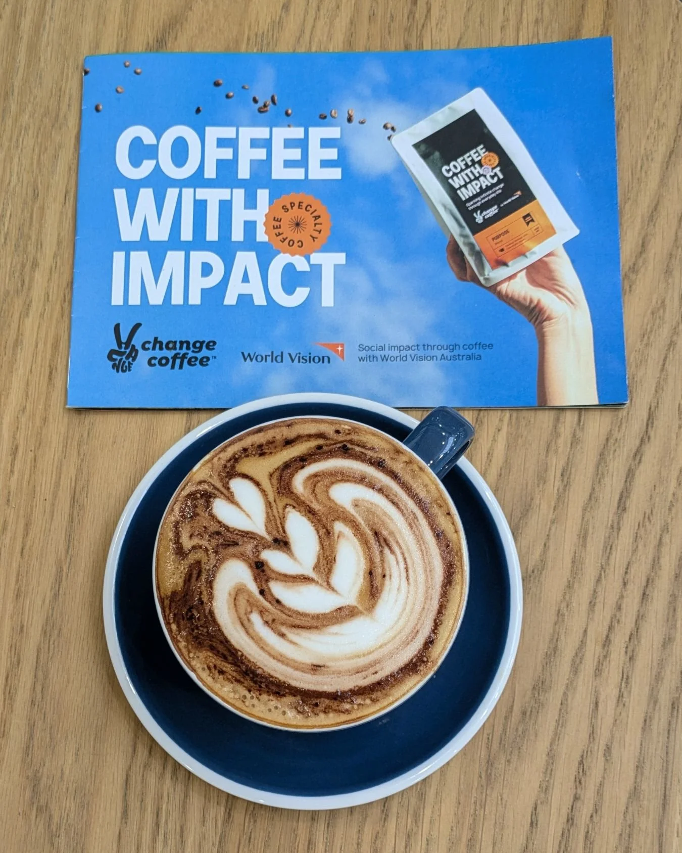 Delicious coffee in a coffee cup sitting on a wooden table with a Change with Impact flyer representing Sarah Marriott's client Change Coffee