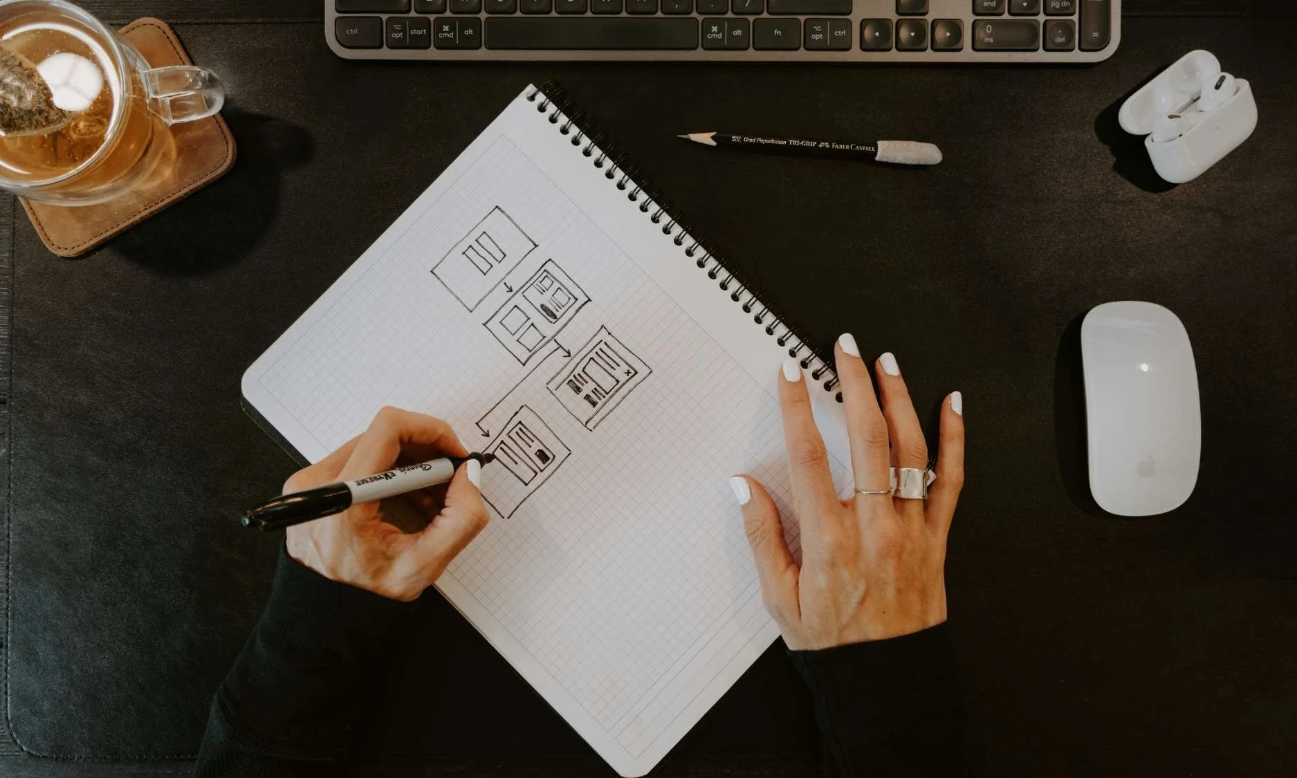 A person sketches a design on paper, focused and surrounded by art supplies in a well-lit workspace