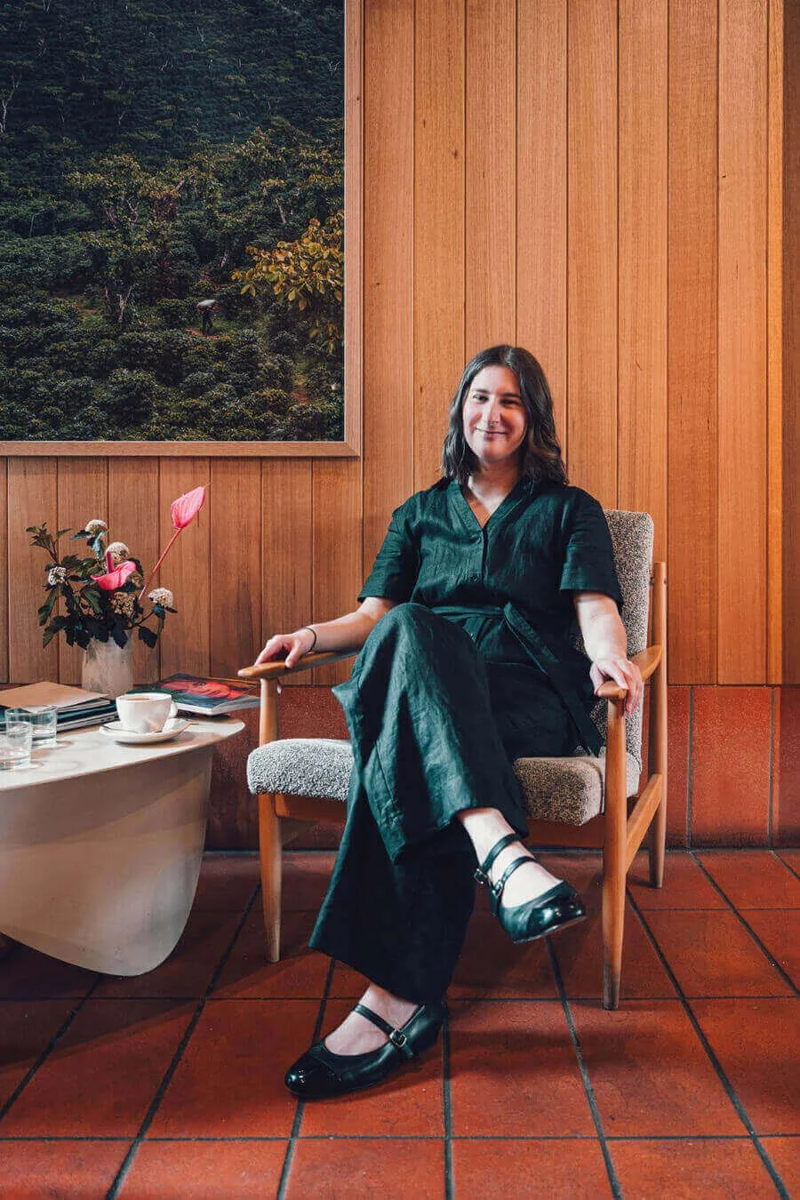 website copywriter Sarah Marriott sitting in cosy cafe smiling at camera wearing black with coffee cup and notebook