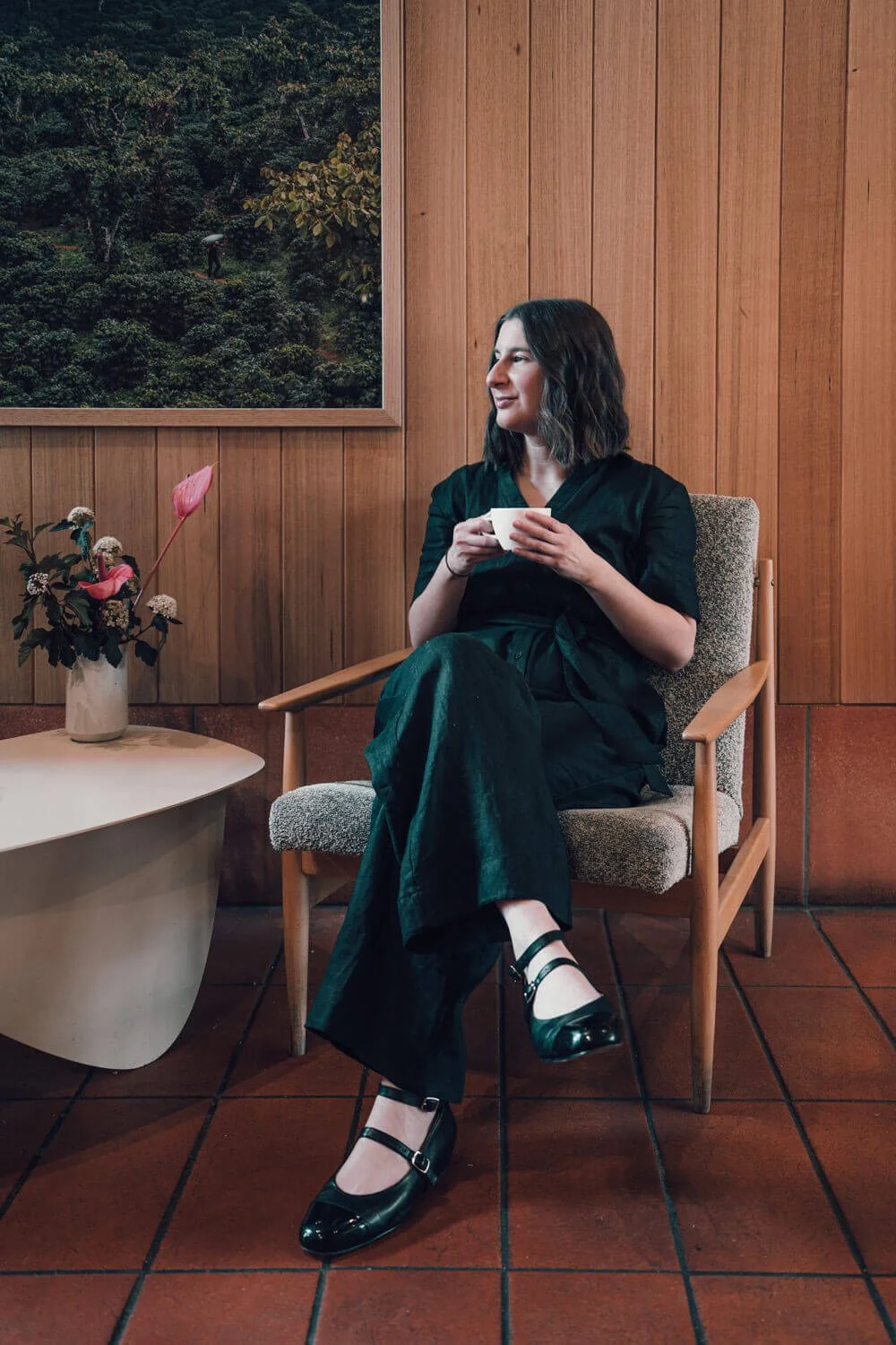 Melbourne copywriter wearing black clothes sitting in a stylish cafe holding a coffee cup at a table with beautiful flowers