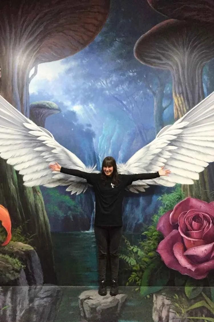 Sarah as a graphic designer at an art gallery standing in front of a painting of angel wings