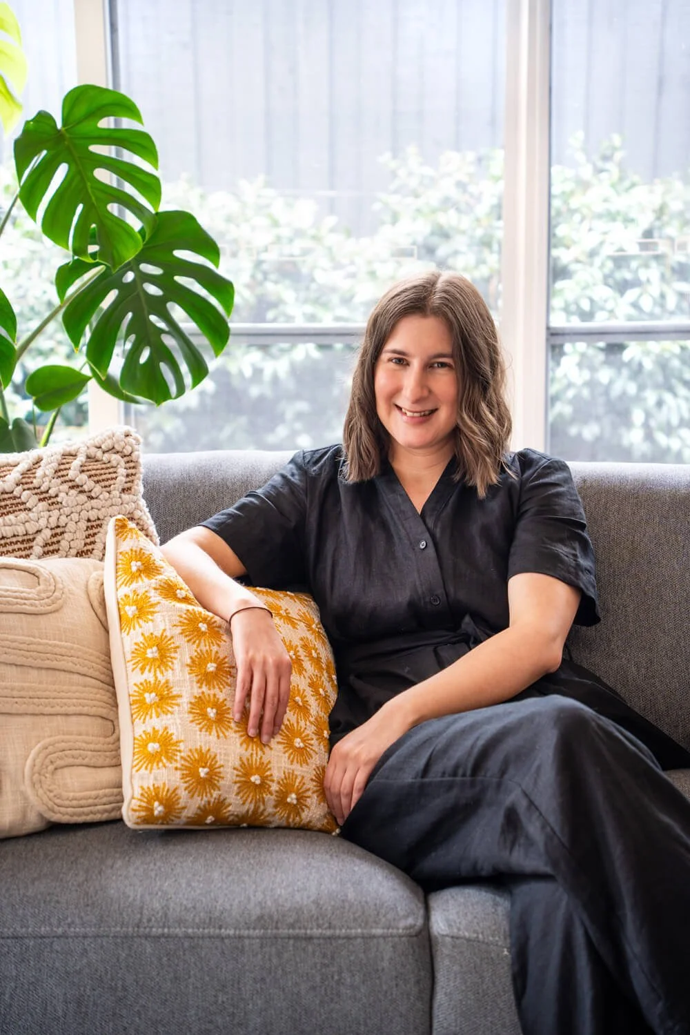 Copywriting services from Sarah Marriott sitting on a grey couch with a friendly smile, wearing black clothes, giving a warm, happy vibe