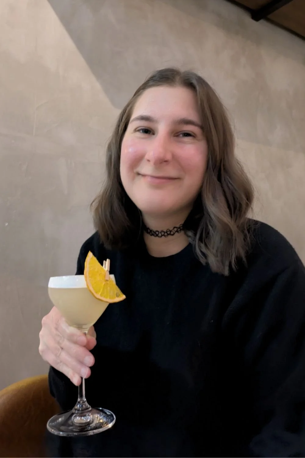 Sarah looking content holding a fancy cocktail at a cosy bar